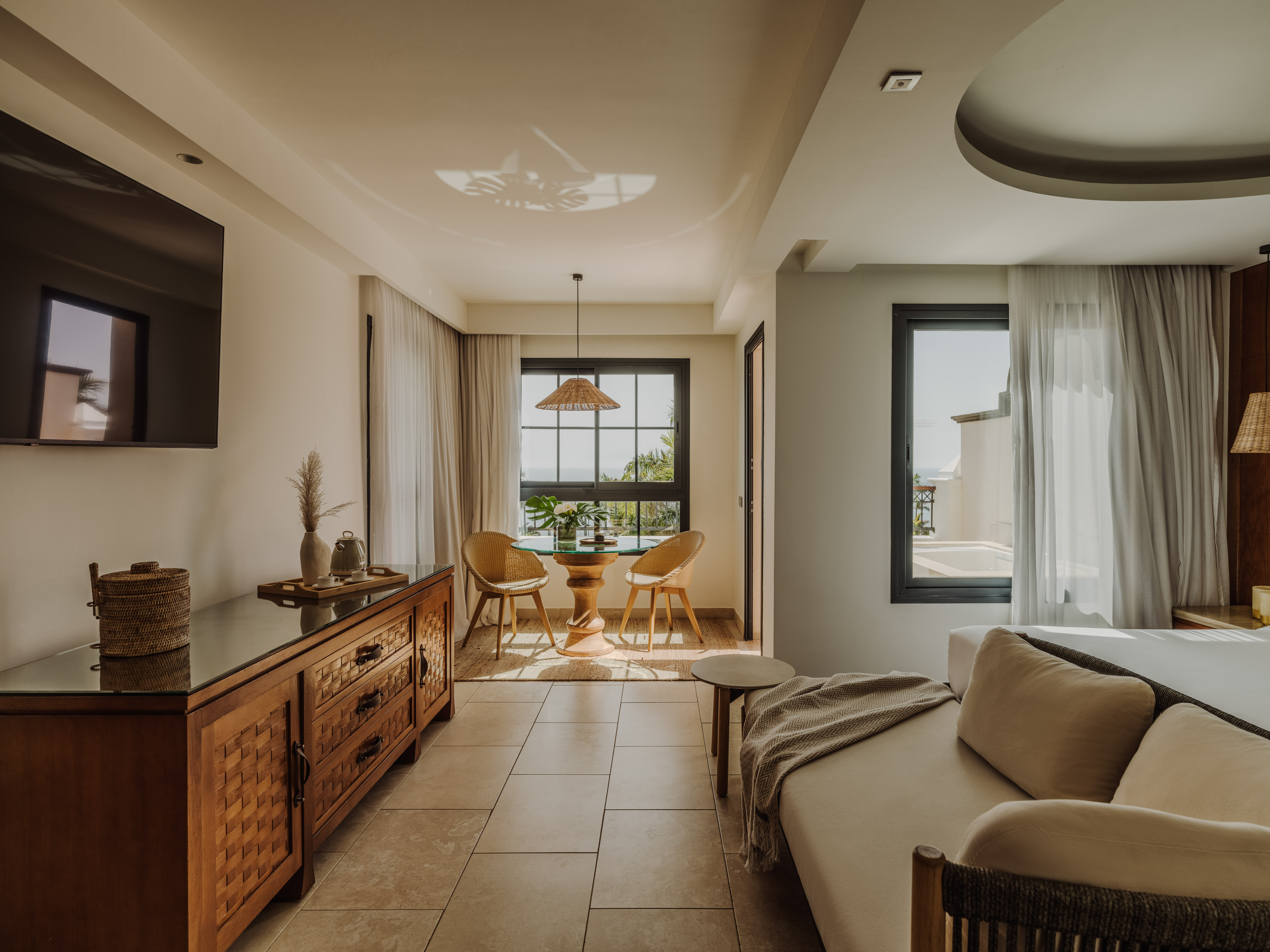 Modern coastal hotel suite with dining table, sofa, and ocean view.