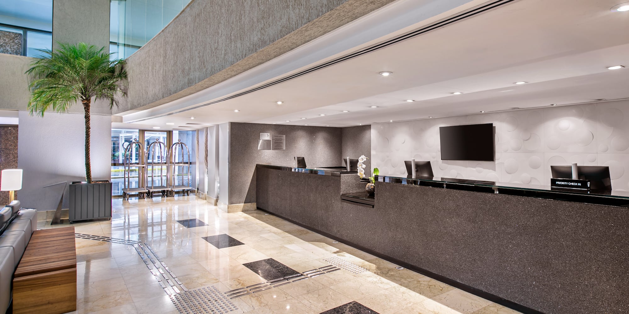 Modern hotel lobby with sleek reception desk, marble floor, and potted palm.