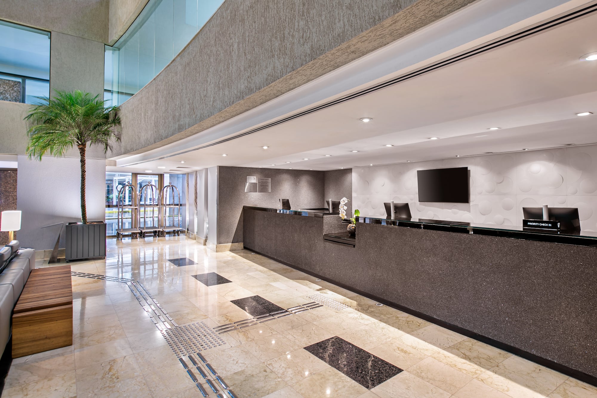 Modern hotel lobby with sleek reception desk, marble floor, and potted palm.