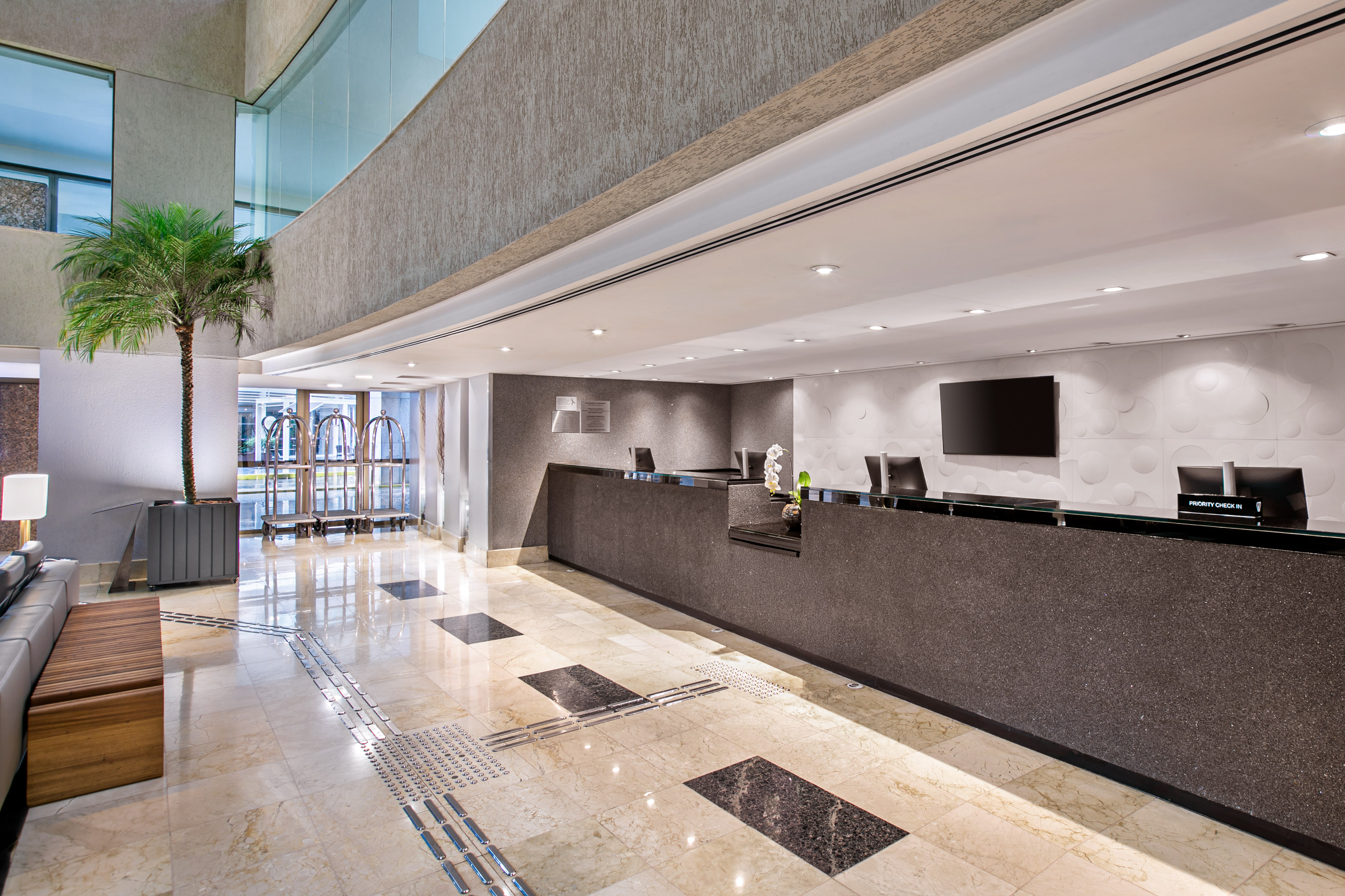 Modern hotel lobby with sleek reception desk, marble floor, and potted palm.