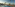 Coastal resort pool with palm trees, sunbeds, beach, and ocean at sunset.