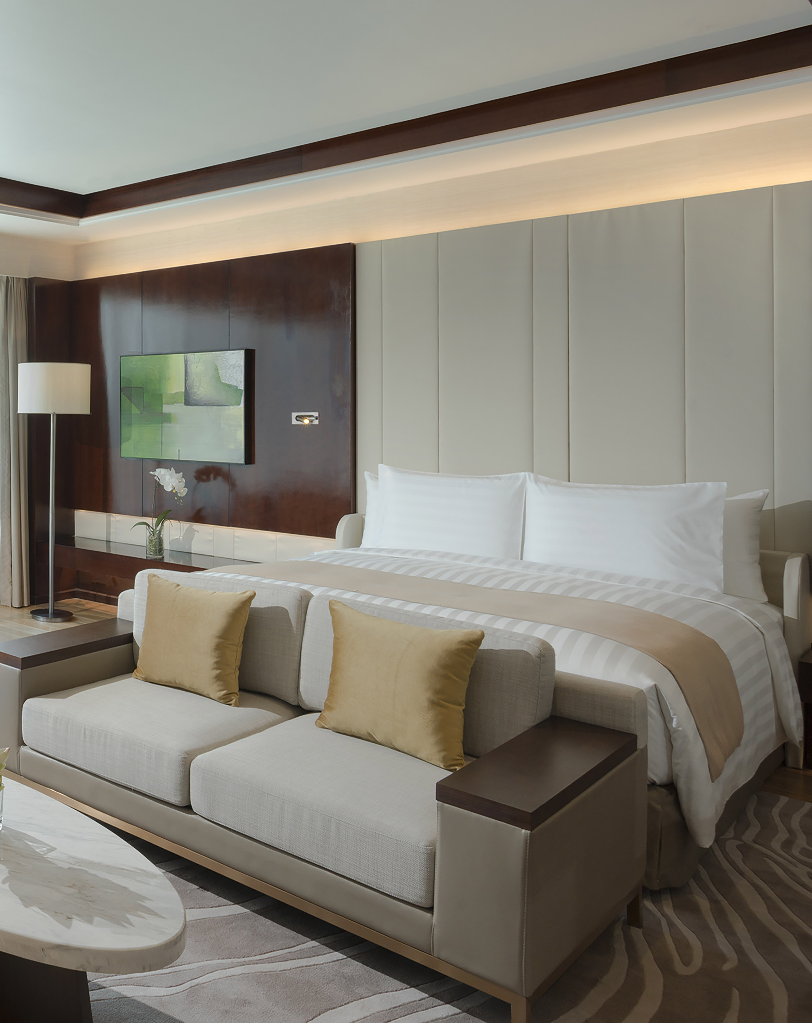 Luxury hotel suite: large bed, elegant dark wood, warm indirect lighting.