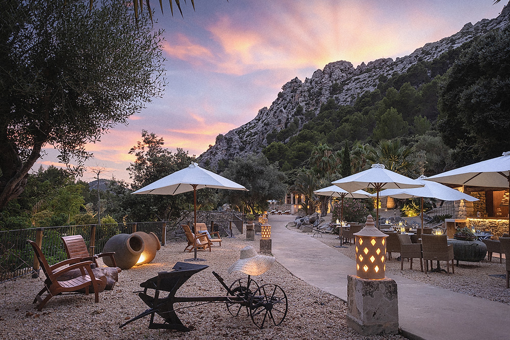 Terraza restaurante exterior en resort con montañas, atardecer y sombrillas.