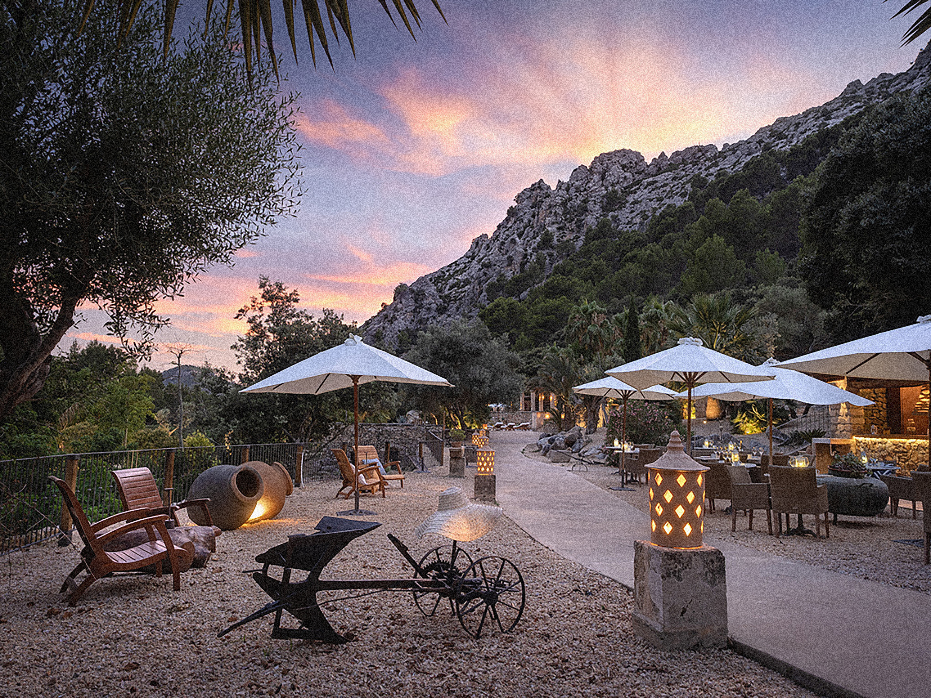 Terraza restaurante exterior en resort con montañas, atardecer y sombrillas.