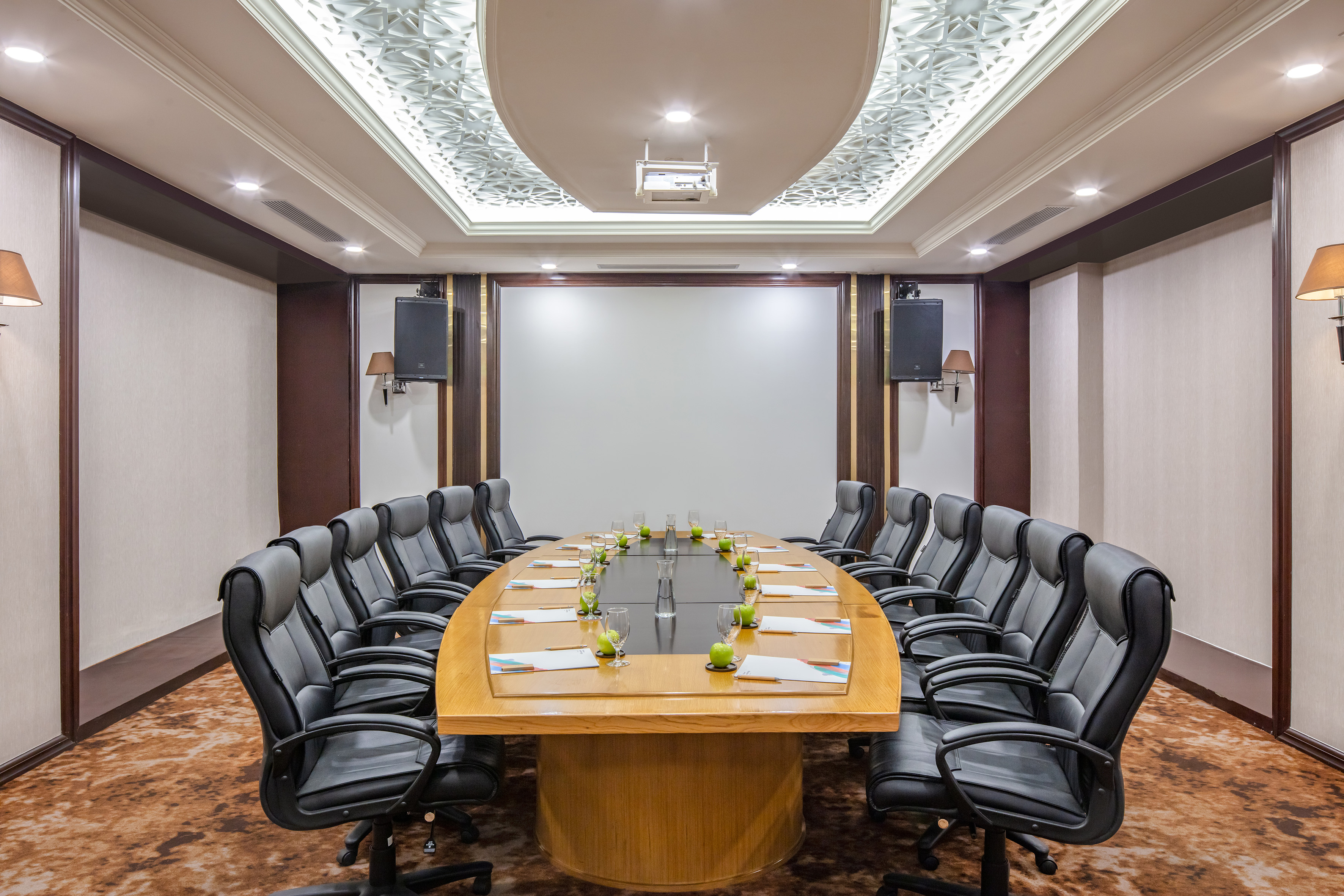 Boardroom with long wood table, black leather chairs, projector, and decorative ceiling.