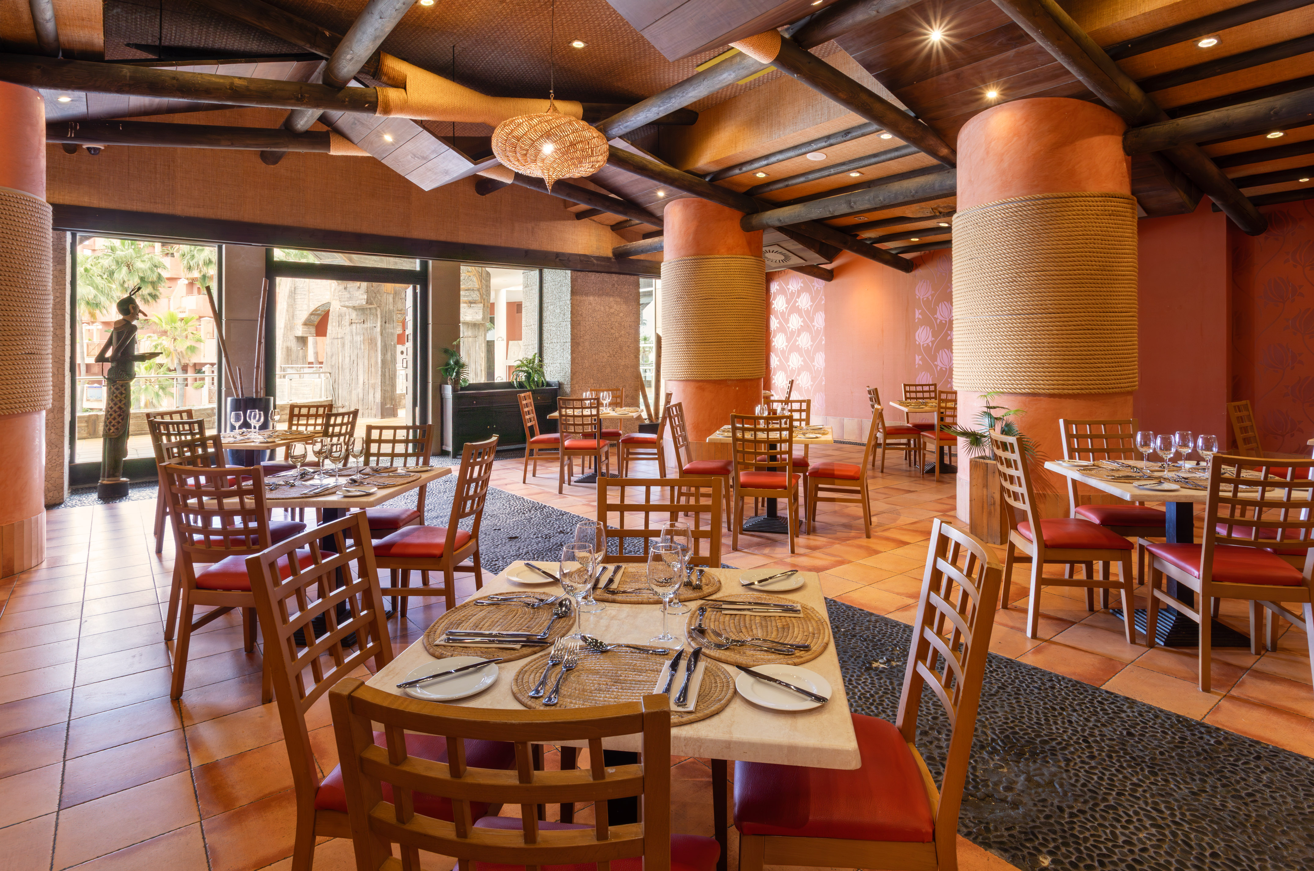 Tropical rustic restaurant dining room with set tables and terracotta floor.