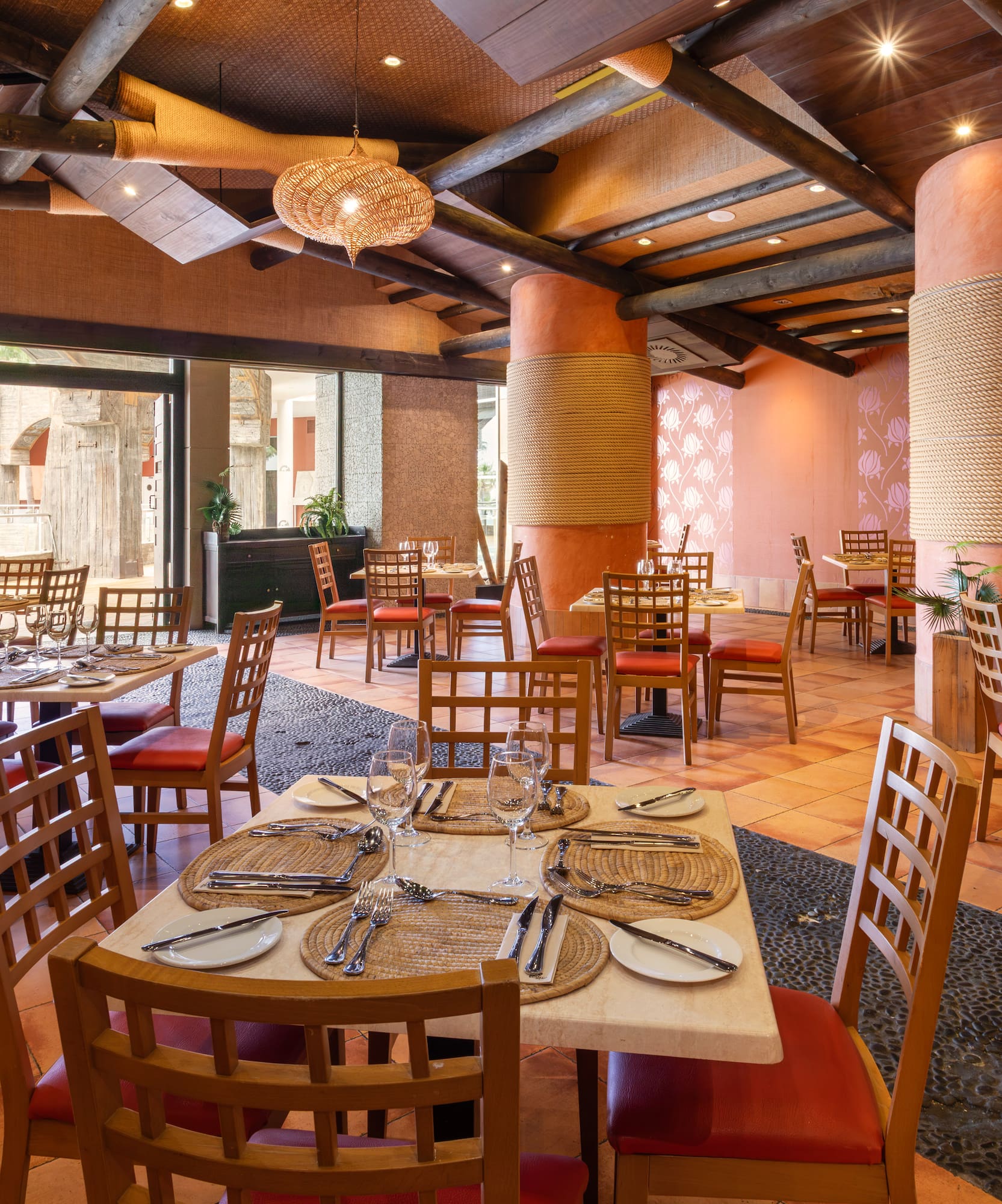 Tropical rustic restaurant dining room with set tables and terracotta floor.