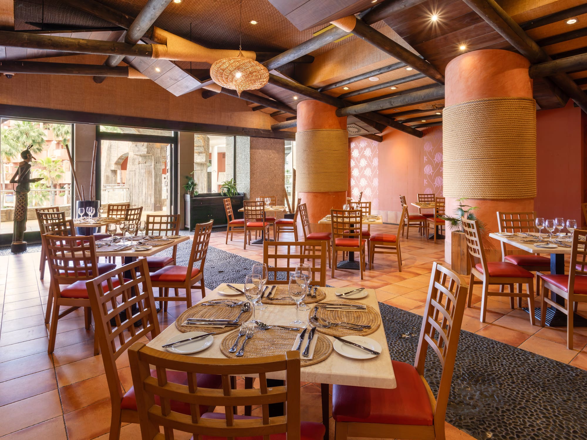 Tropical resort restaurant dining room, set tables, red chairs, warm decor.