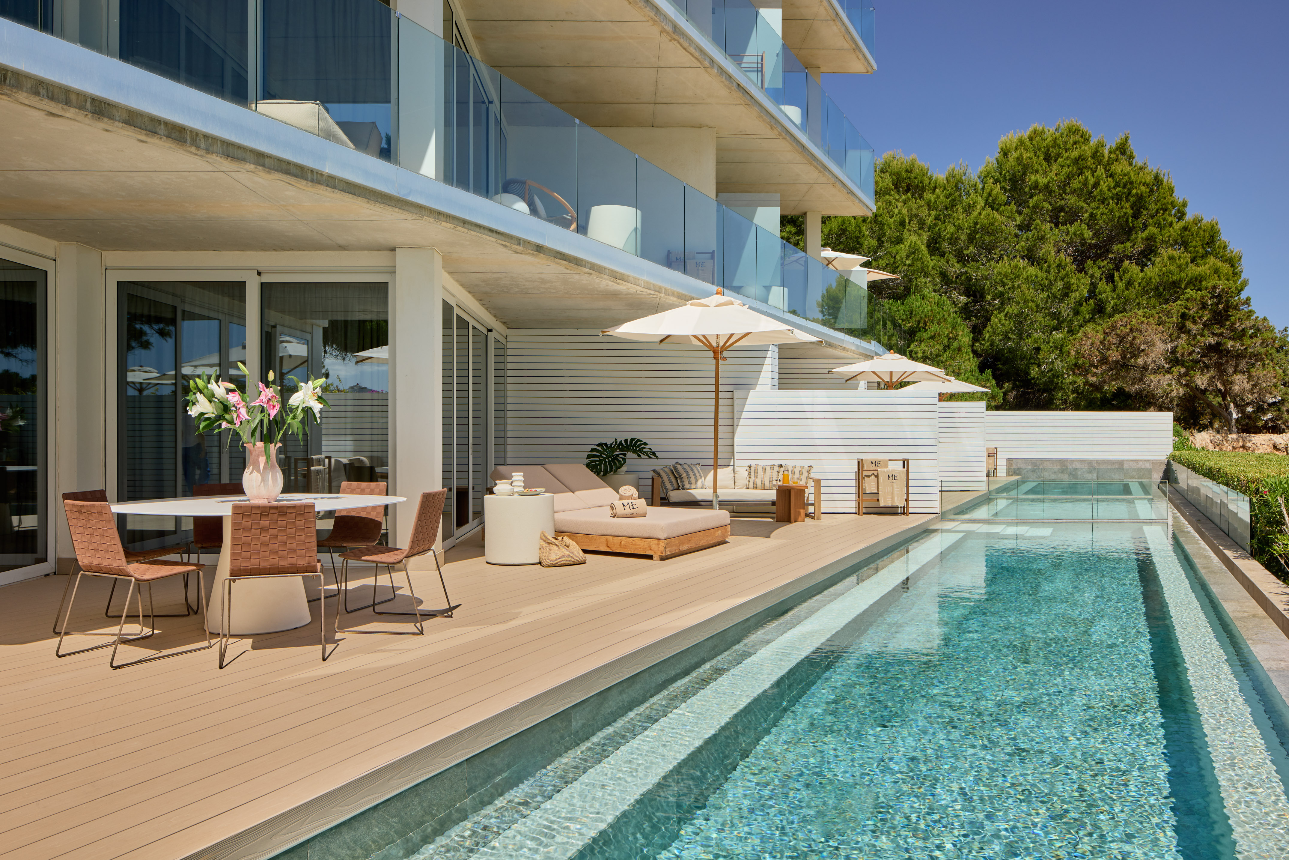 Modern resort terrace with pool, dining, and sun loungers under balconies.