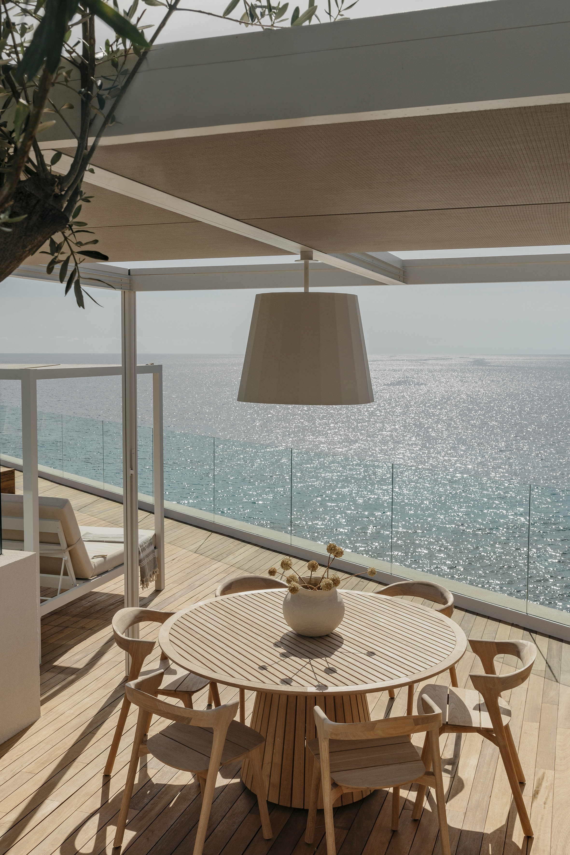 Wooden outdoor dining set on a balcony with sparkling sea view.