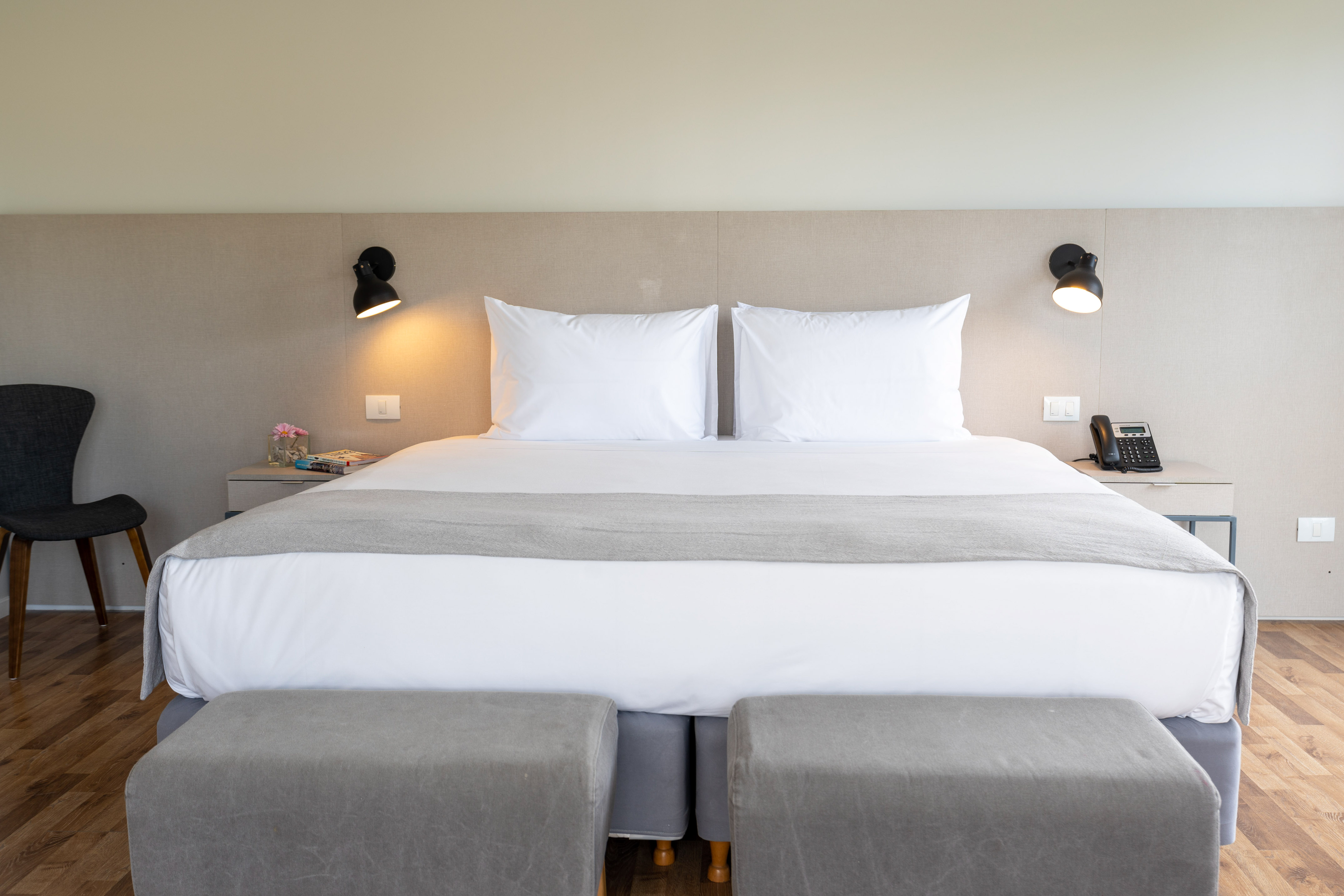 Modern hotel bedroom with king bed, white linens, gray accents, and wall lights.
