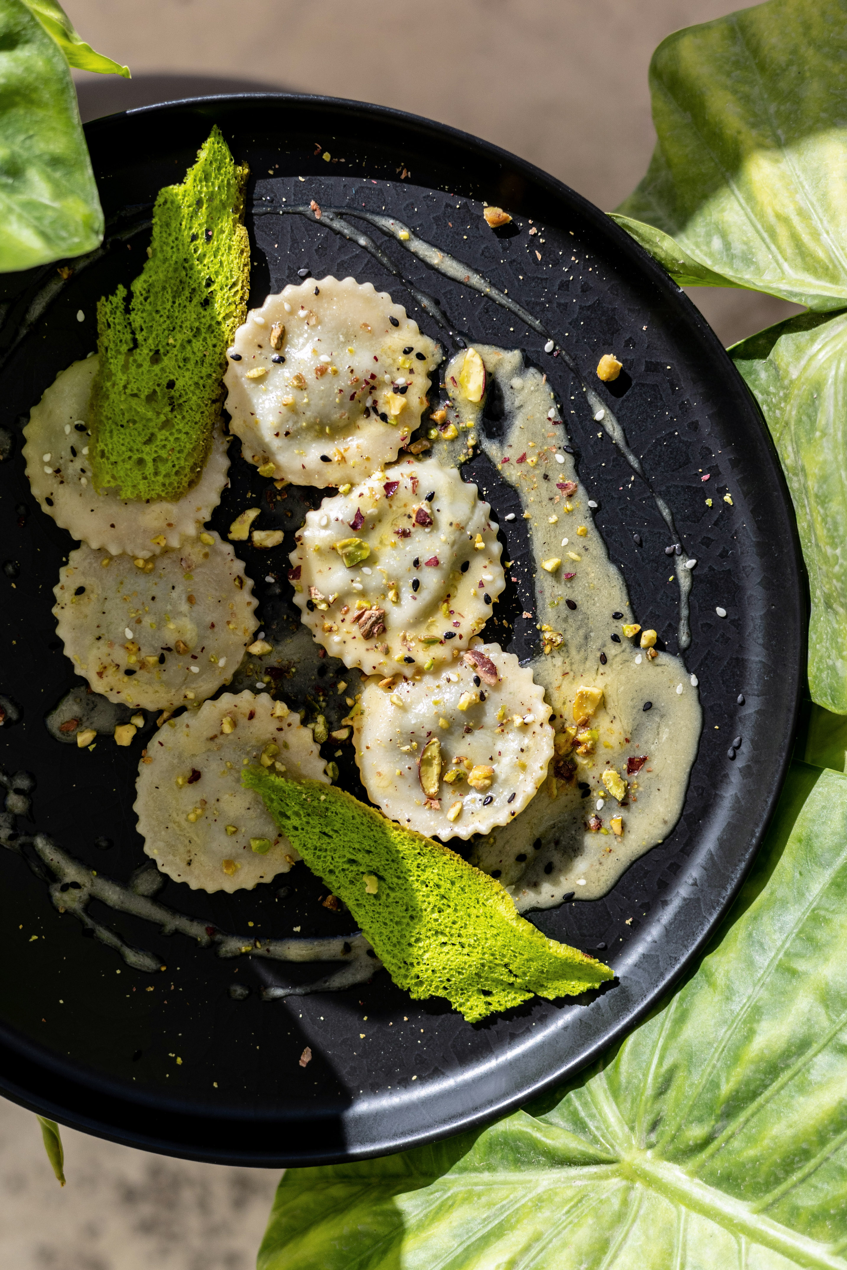Gourmet ravioli with pistachios, sesame, green sauce, and crispy tuile on black plate. - Restaurant Amadeo, Aperitieven - Hotel Vlora Priam Affiliated by Meliá, Vlora
