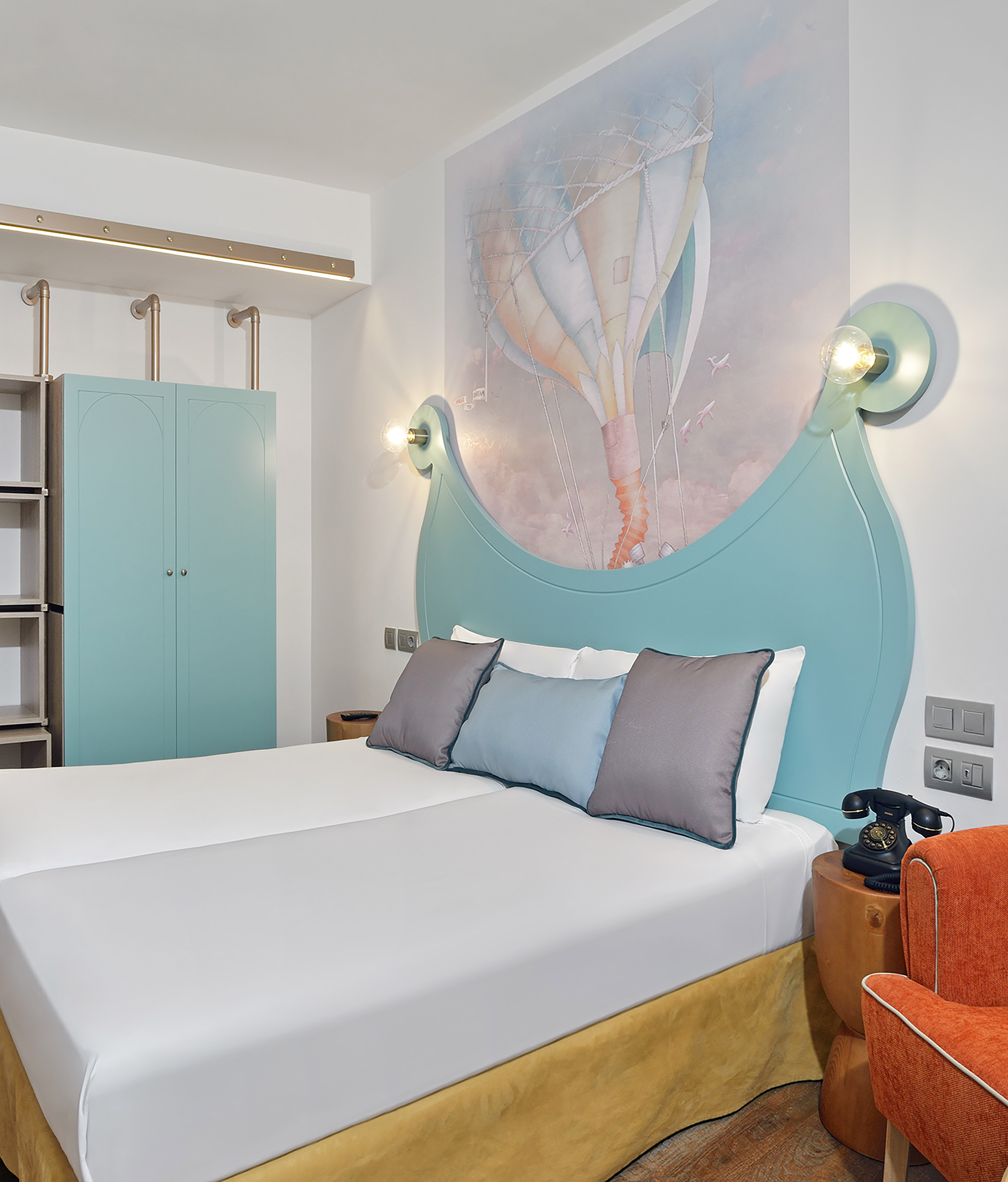 Modern hotel bedroom with hot air balloon mural and turquoise headboard.