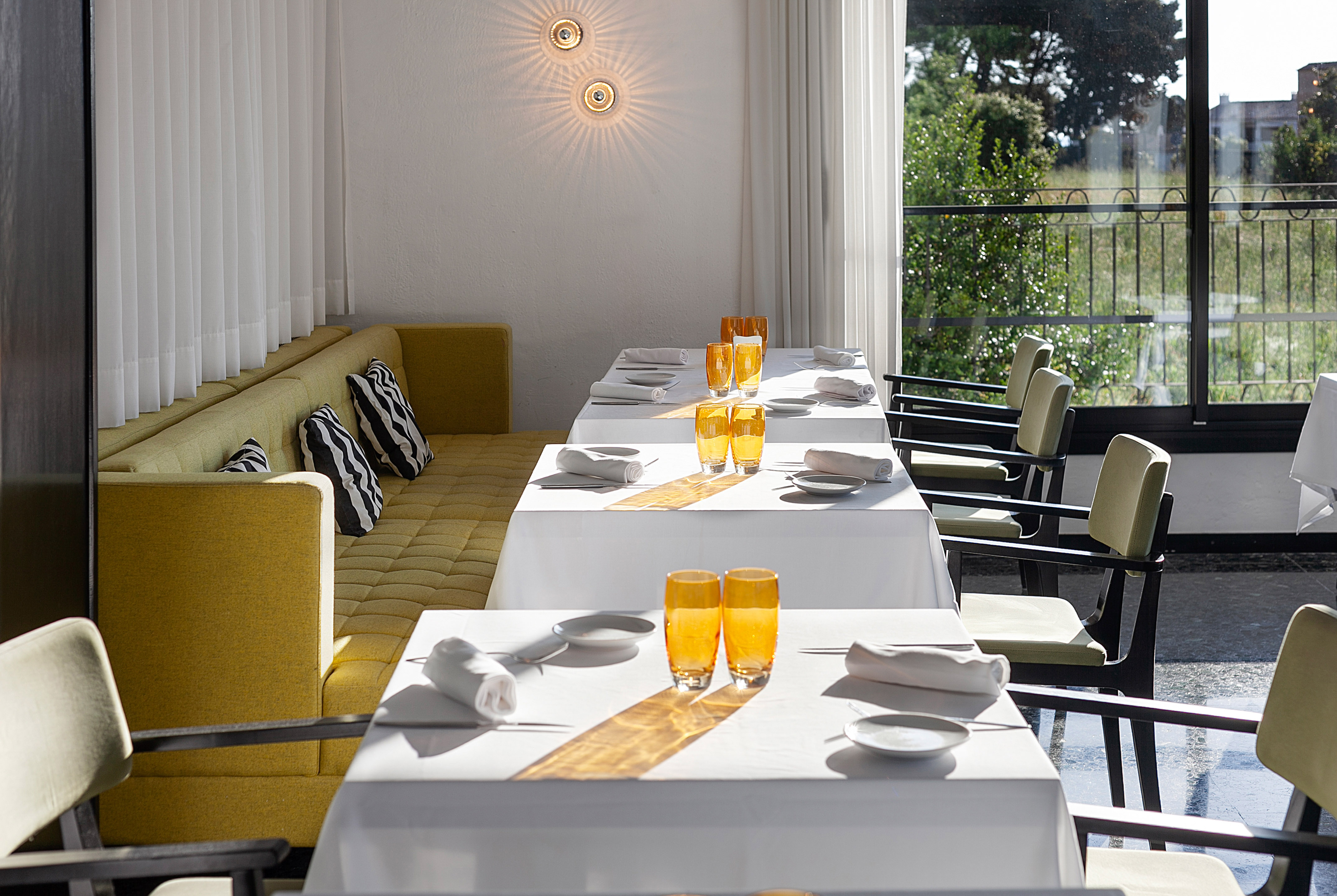 Modern restaurant dining room with yellow banquette seating and sunlit tables.