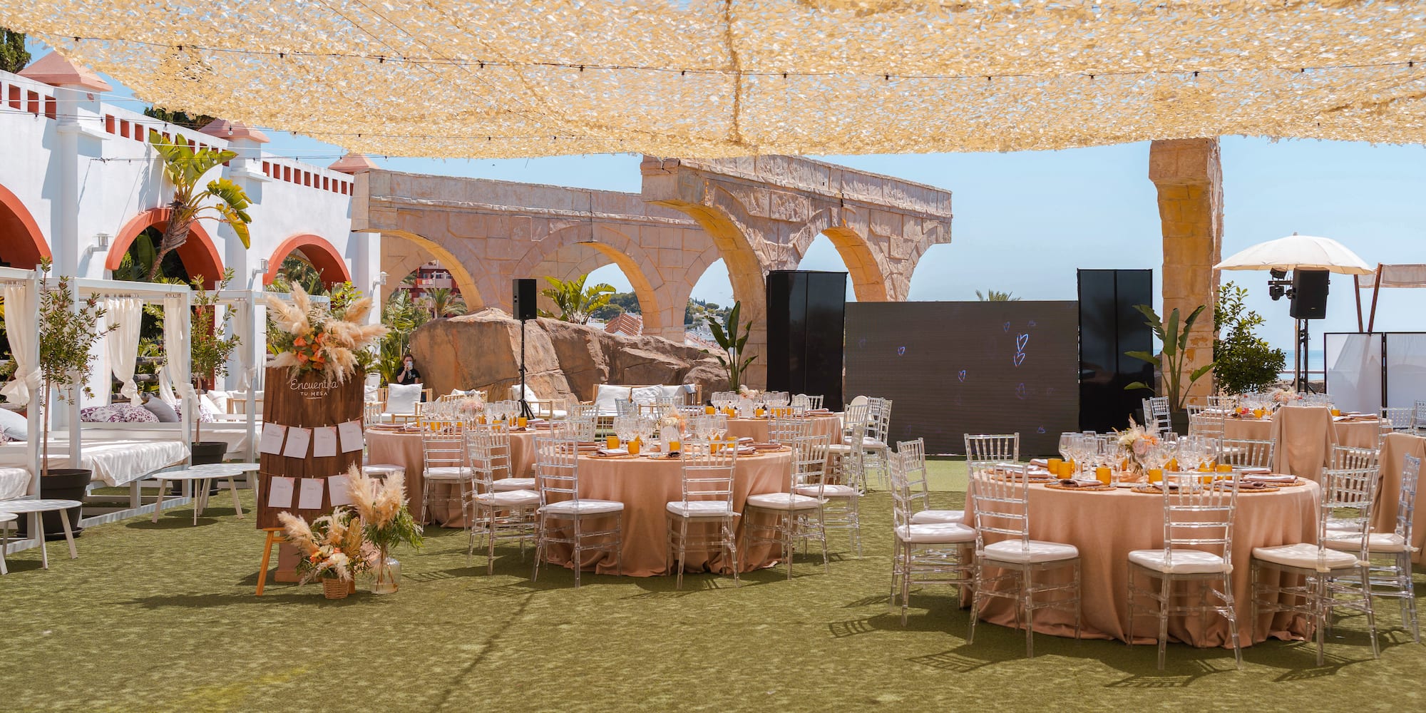 Outdoor reception tables, ghost chairs, pampas grass decor, and stone arches.