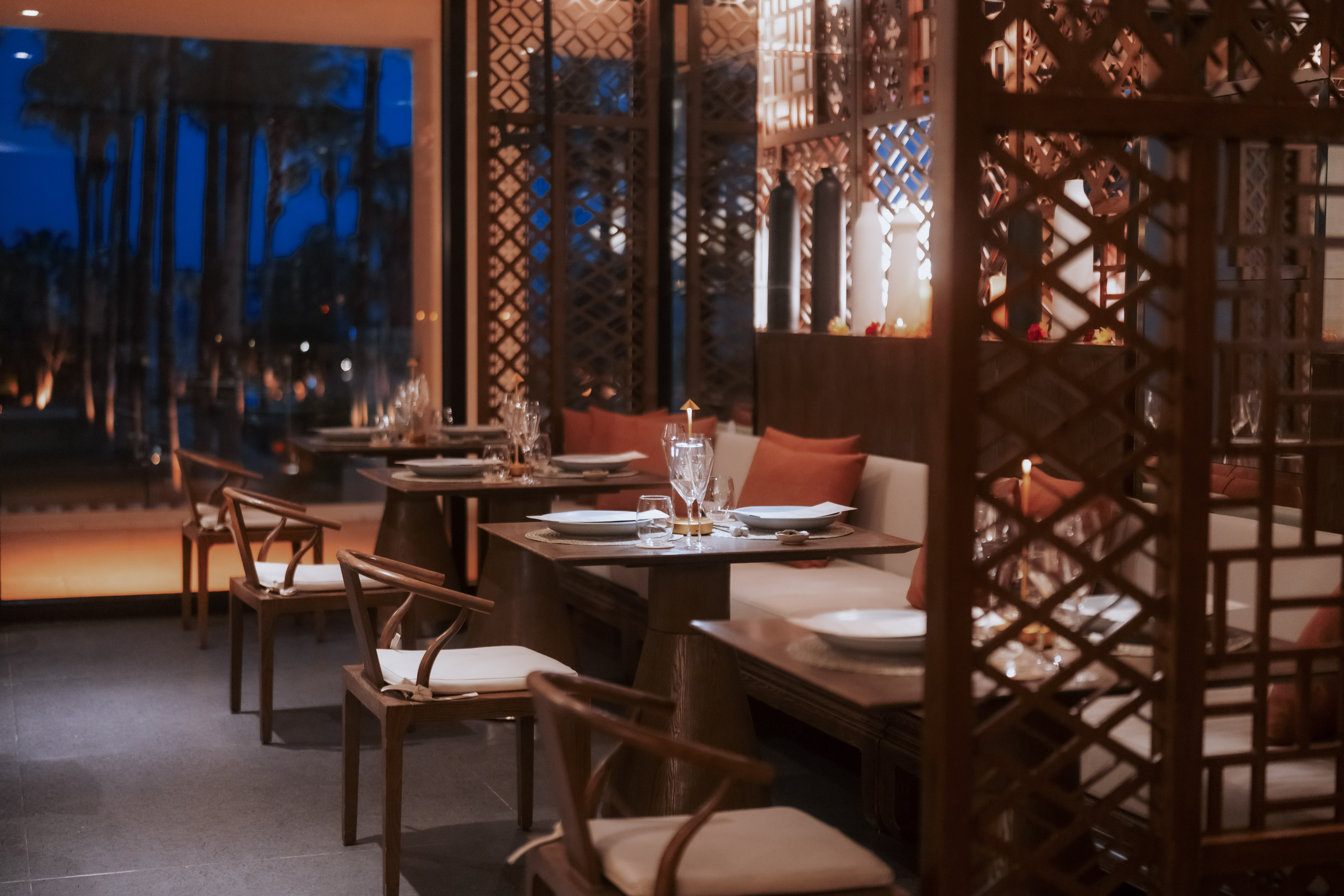Elegant restaurant dining room with set tables, wooden screens, and evening view.