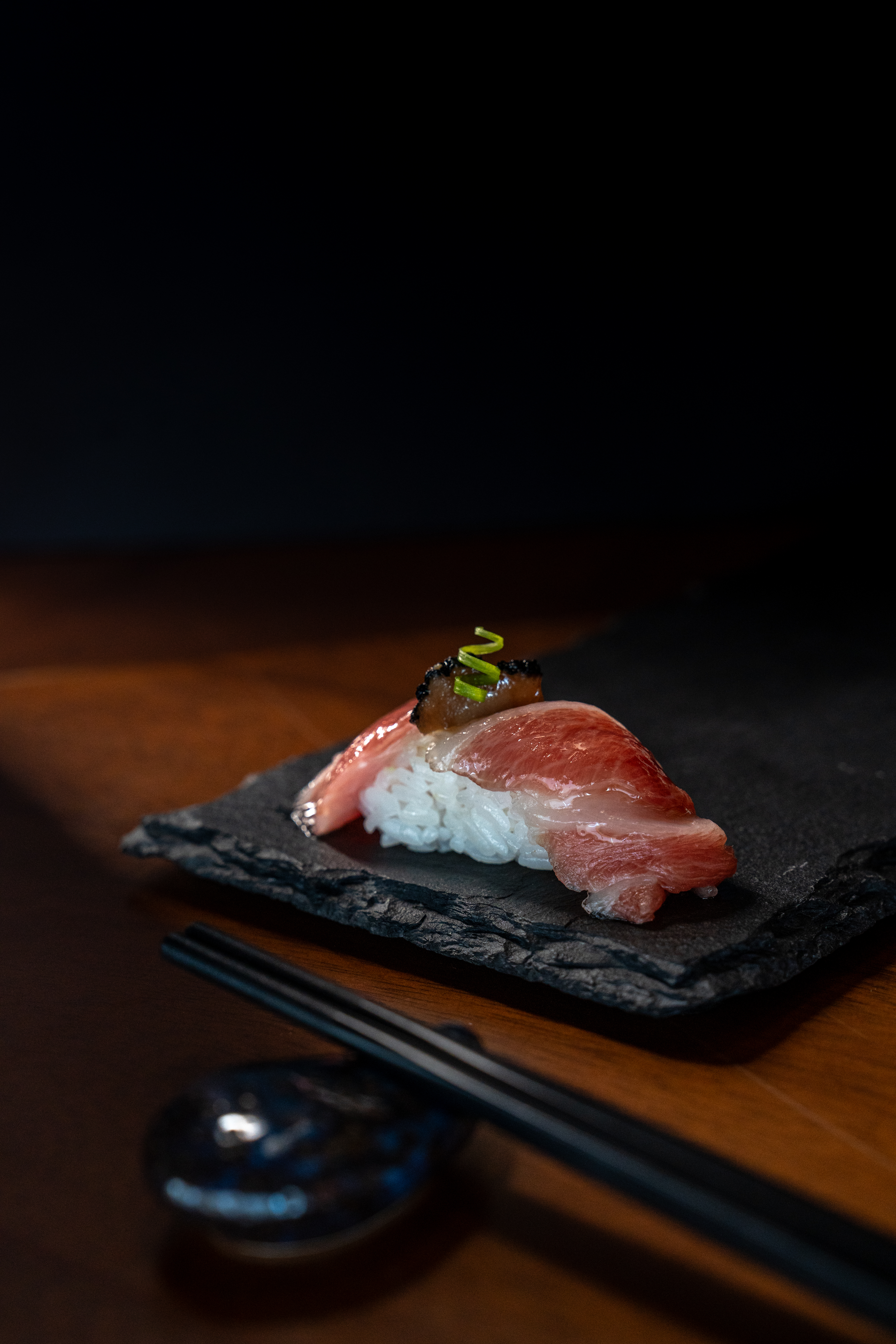Marbled tuna nigiri sushi with green garnish on slate and chopsticks.
