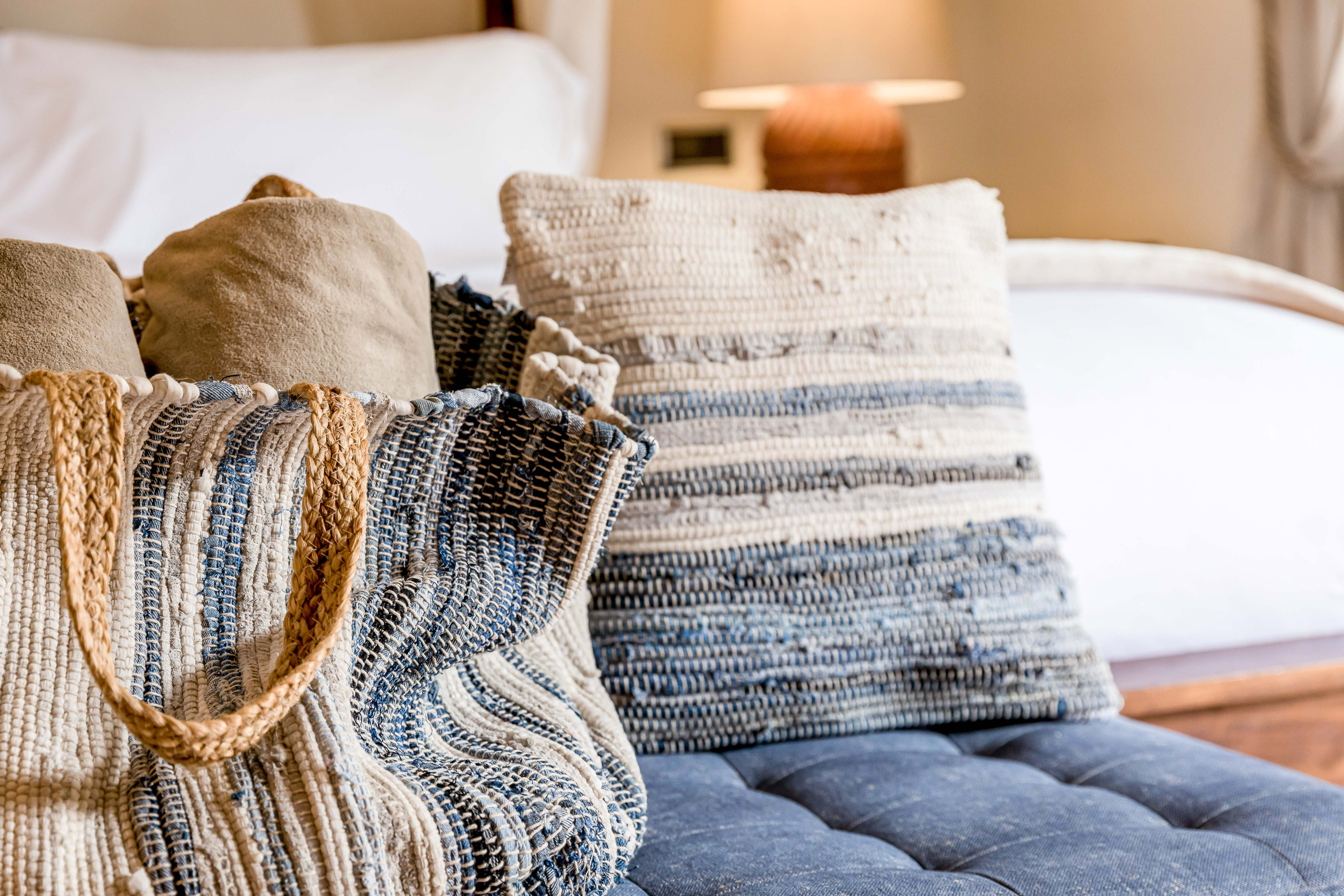 Woven blue/natural tote bag with textured pillow on tufted blue bench.