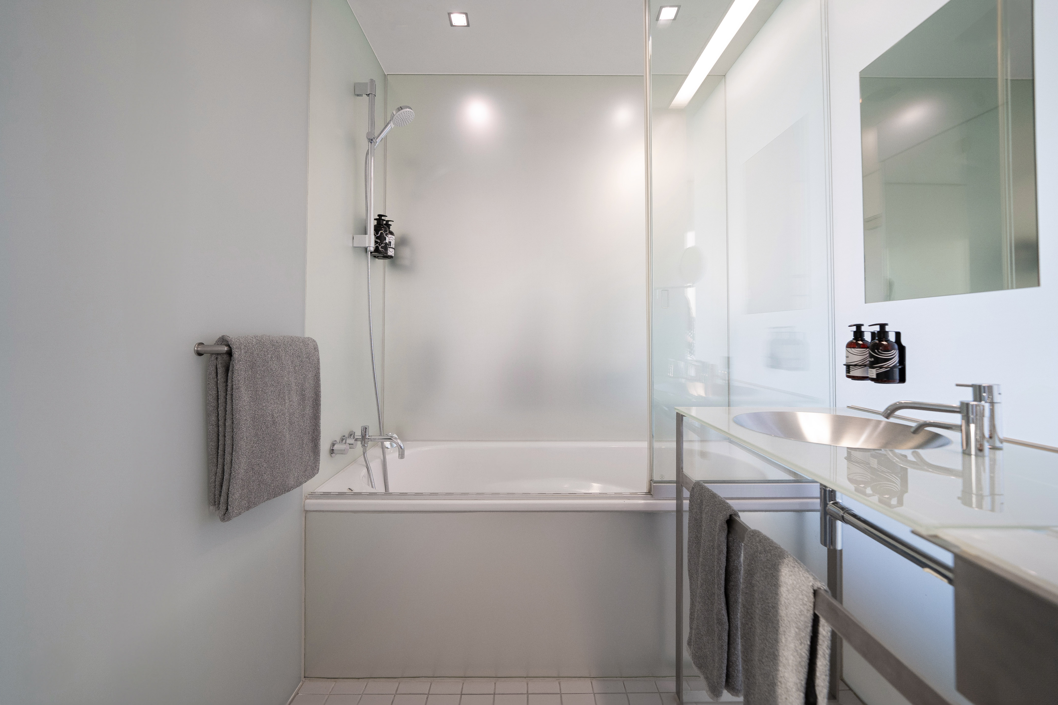 Modern bathroom with white bathtub, glass shower, and minimalist vanity sink.