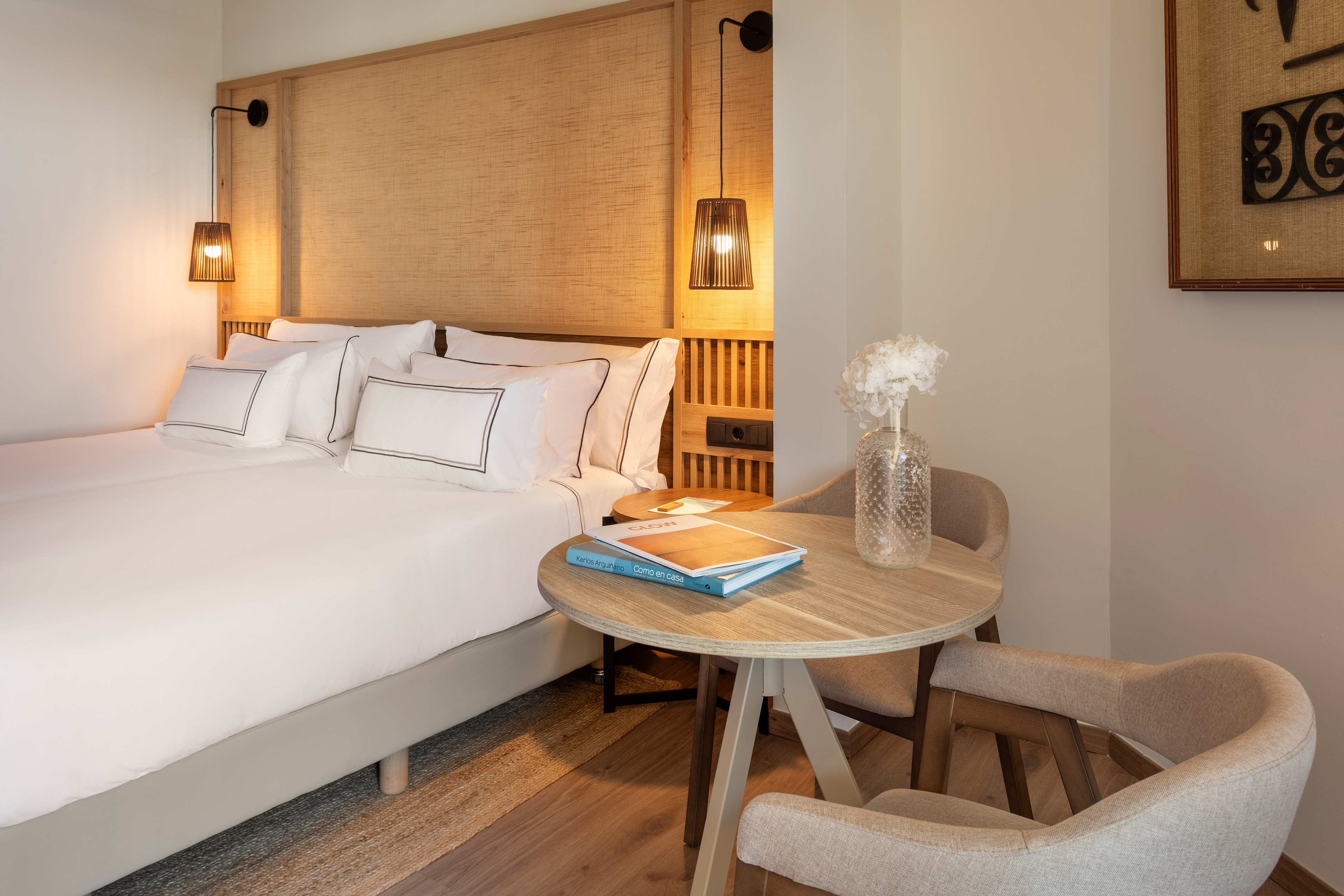 Cozy hotel room with wooden headboard, bright white bedding, and small table for two.