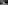 Black and white: Woman in jumpsuit rides bicycle with front basket on a street.