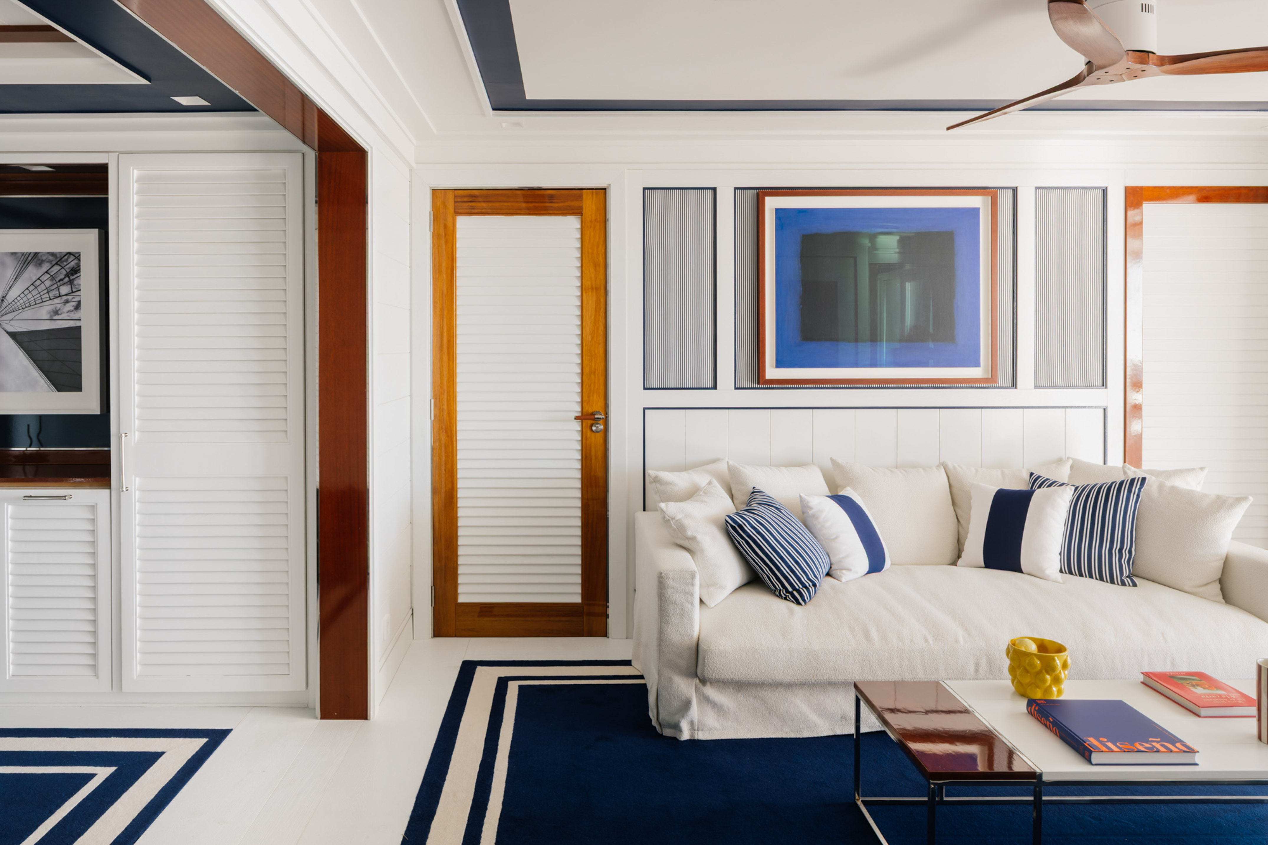 White living room, blue & white rug, sofa, abstract art, wood accents.