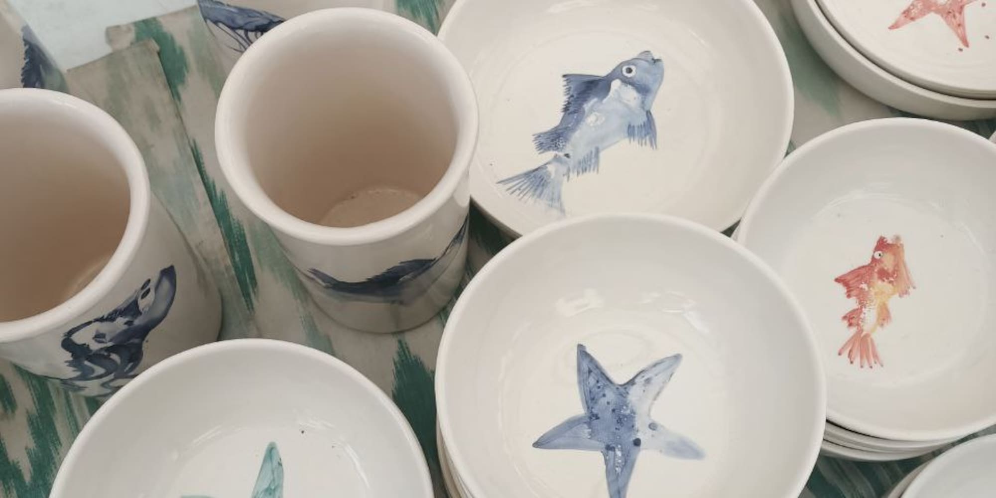 a group of bowls and mugs with fish and starfish painted on them