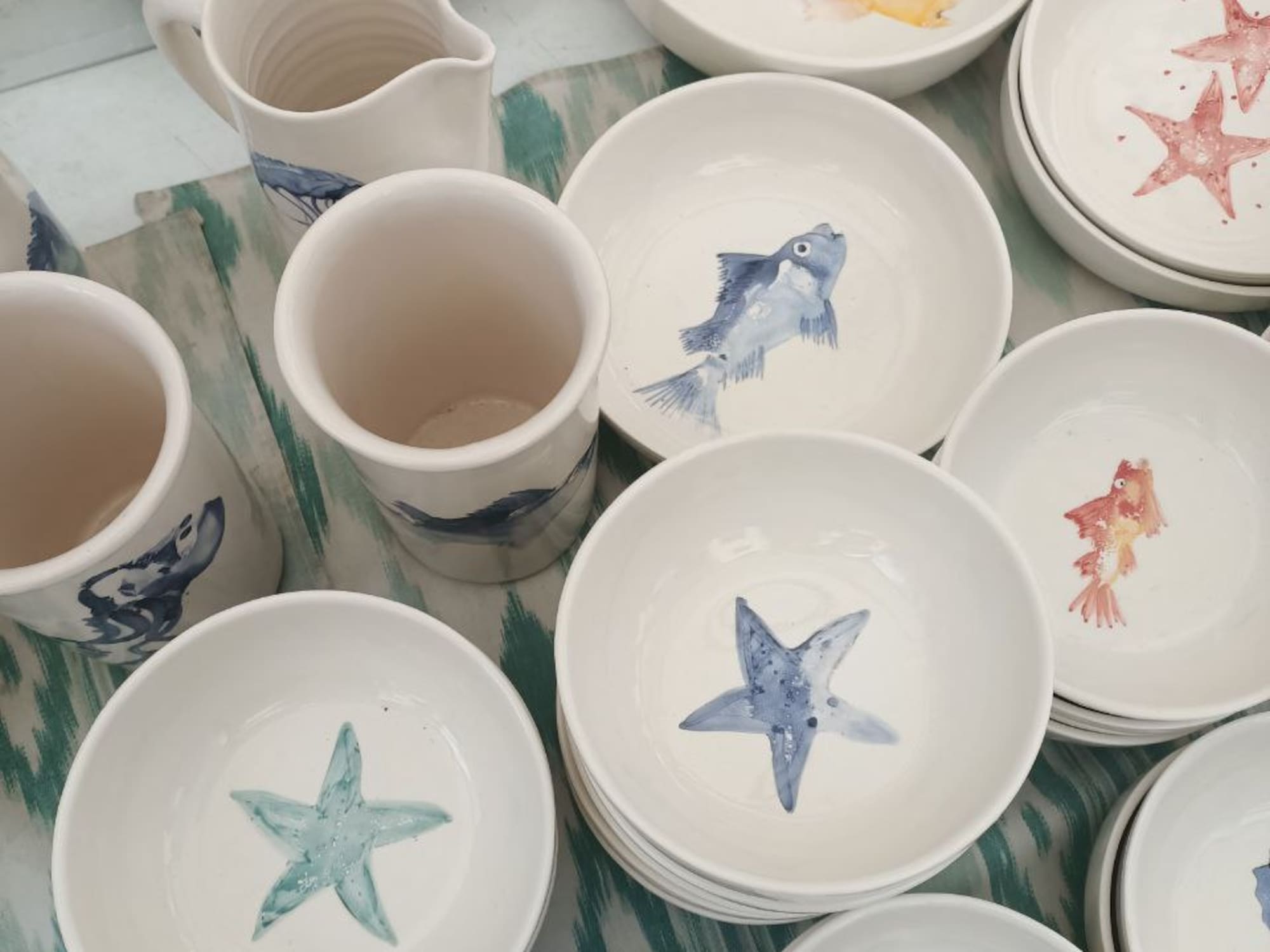 a group of bowls and mugs with fish and starfish painted on them