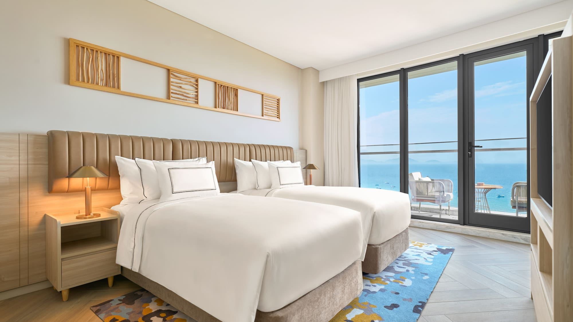 Modern hotel room with twin beds and ocean view balcony.