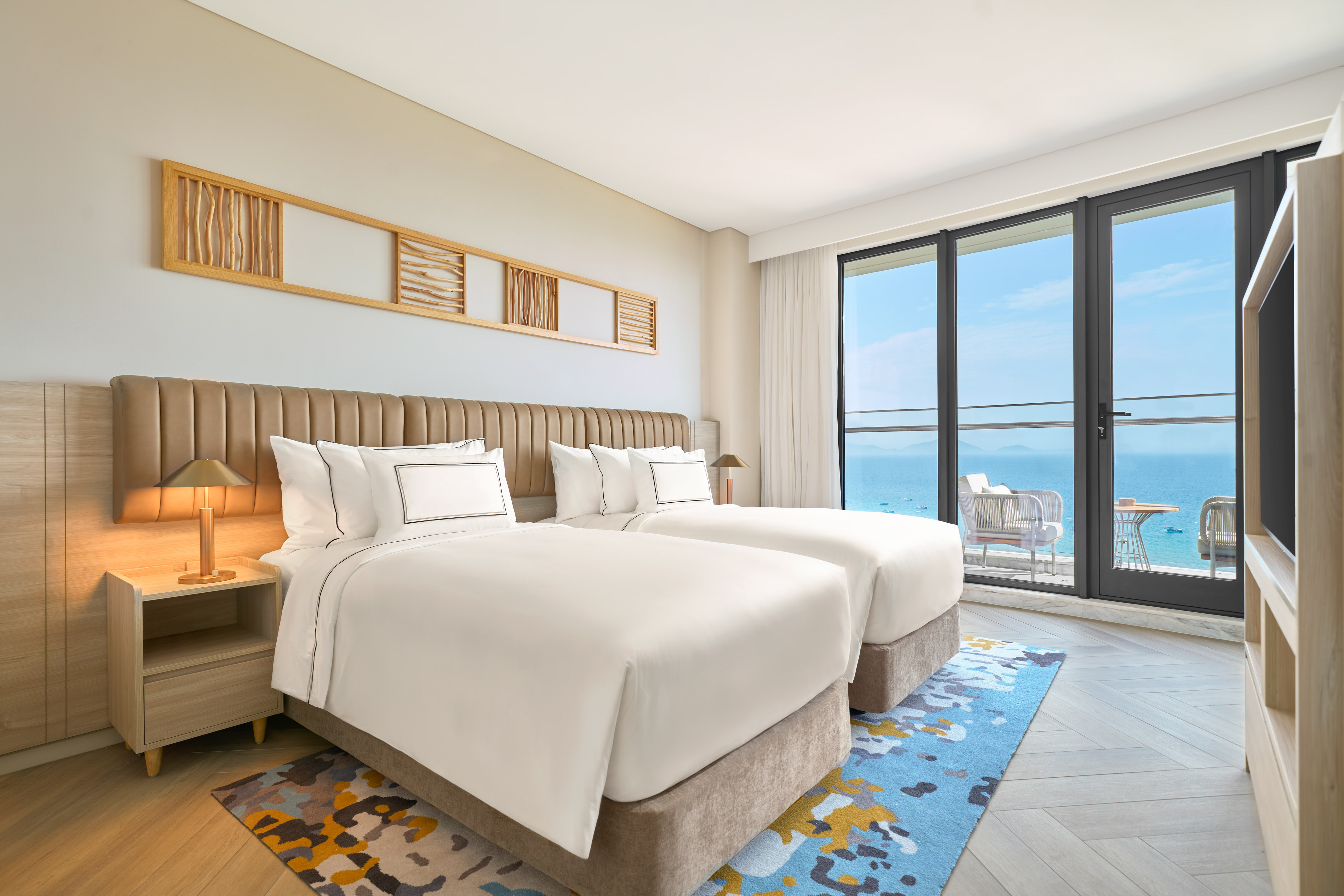 Modern hotel room with twin beds and ocean view balcony.