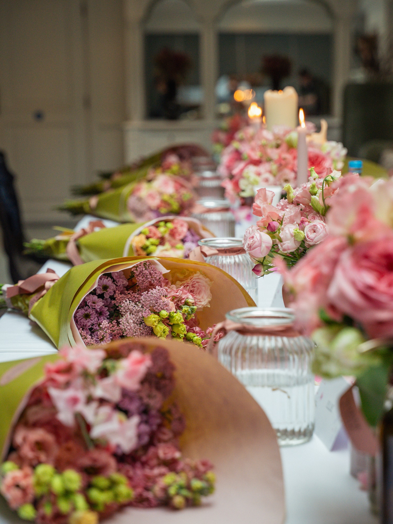Pink and purple wrapped flower bouquets lined on an elegant table with candles.