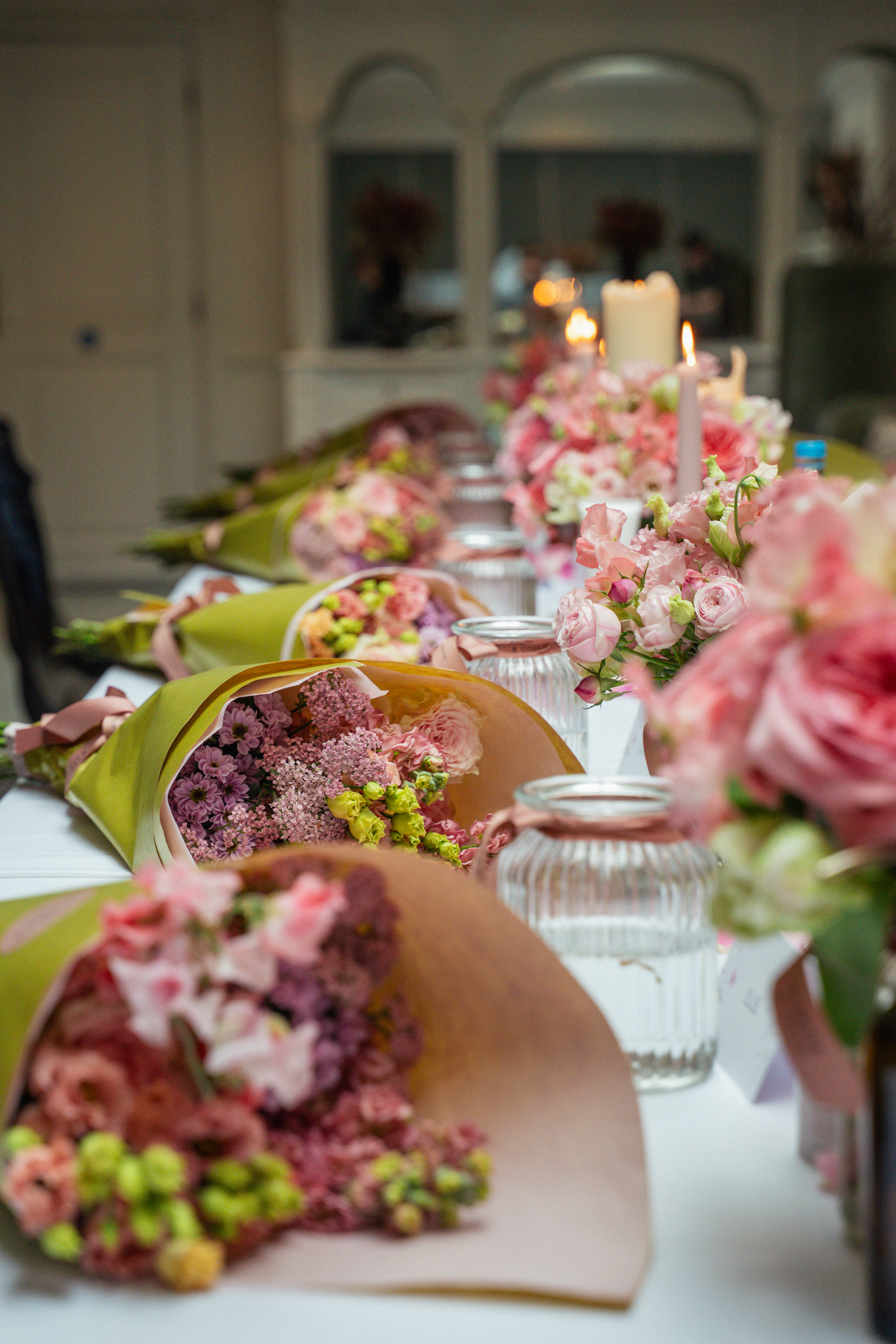 Pink and purple wrapped flower bouquets lined on an elegant table with candles.