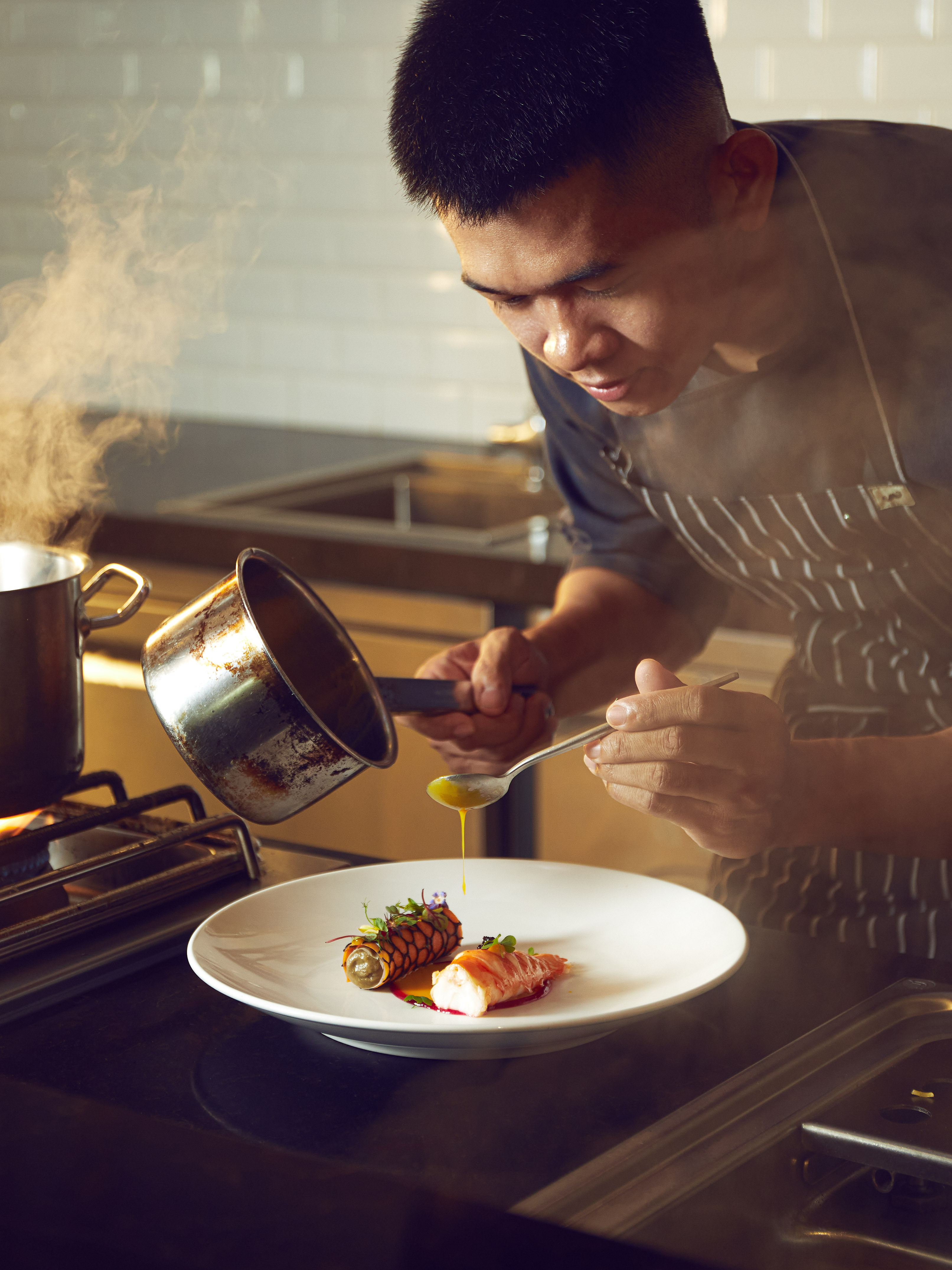 Chef plating gourmet meal, drizzling yellow sauce onto a white plate.