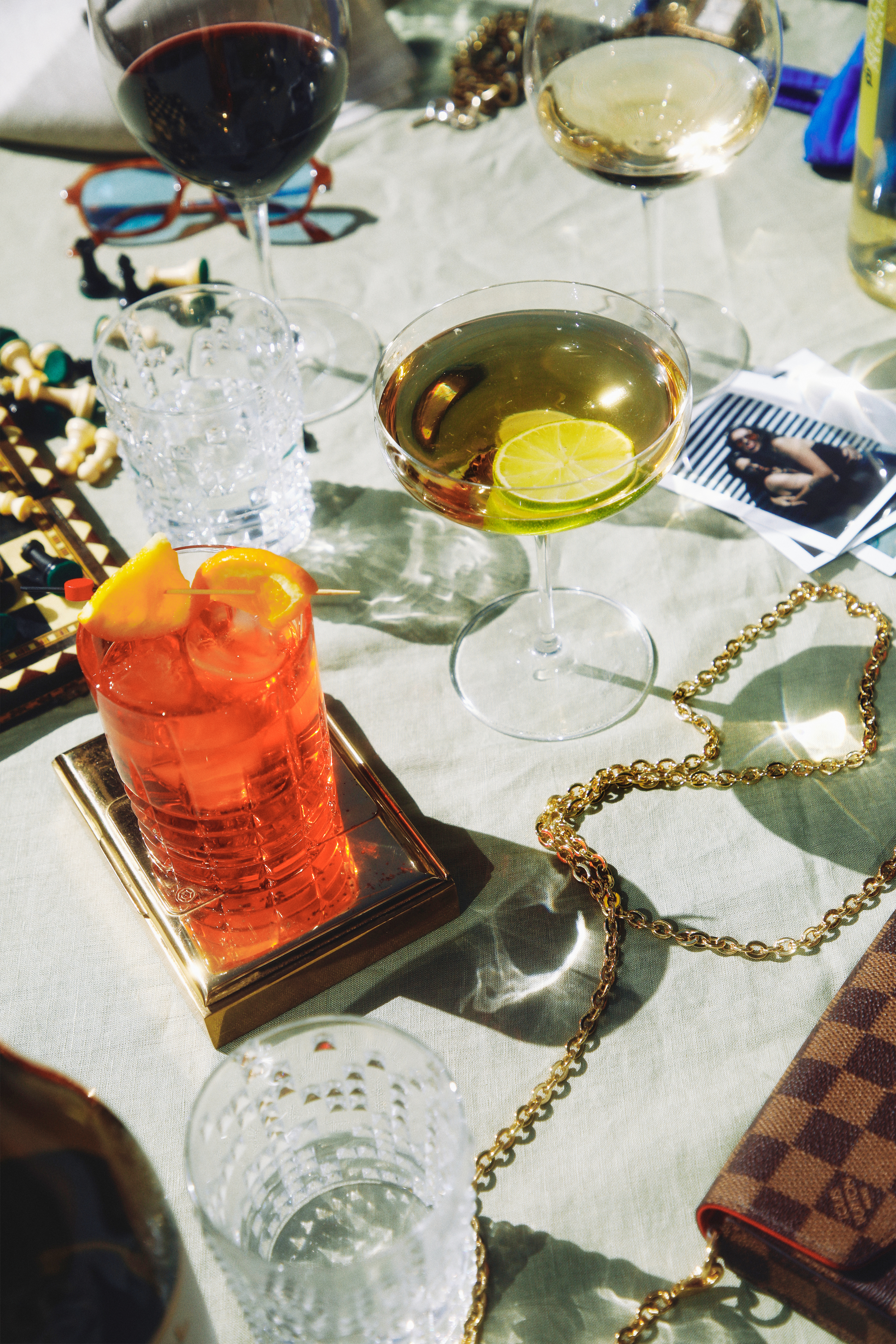 Assorted cocktails, wine, gold chain, and luxury clutch on a stylish table.