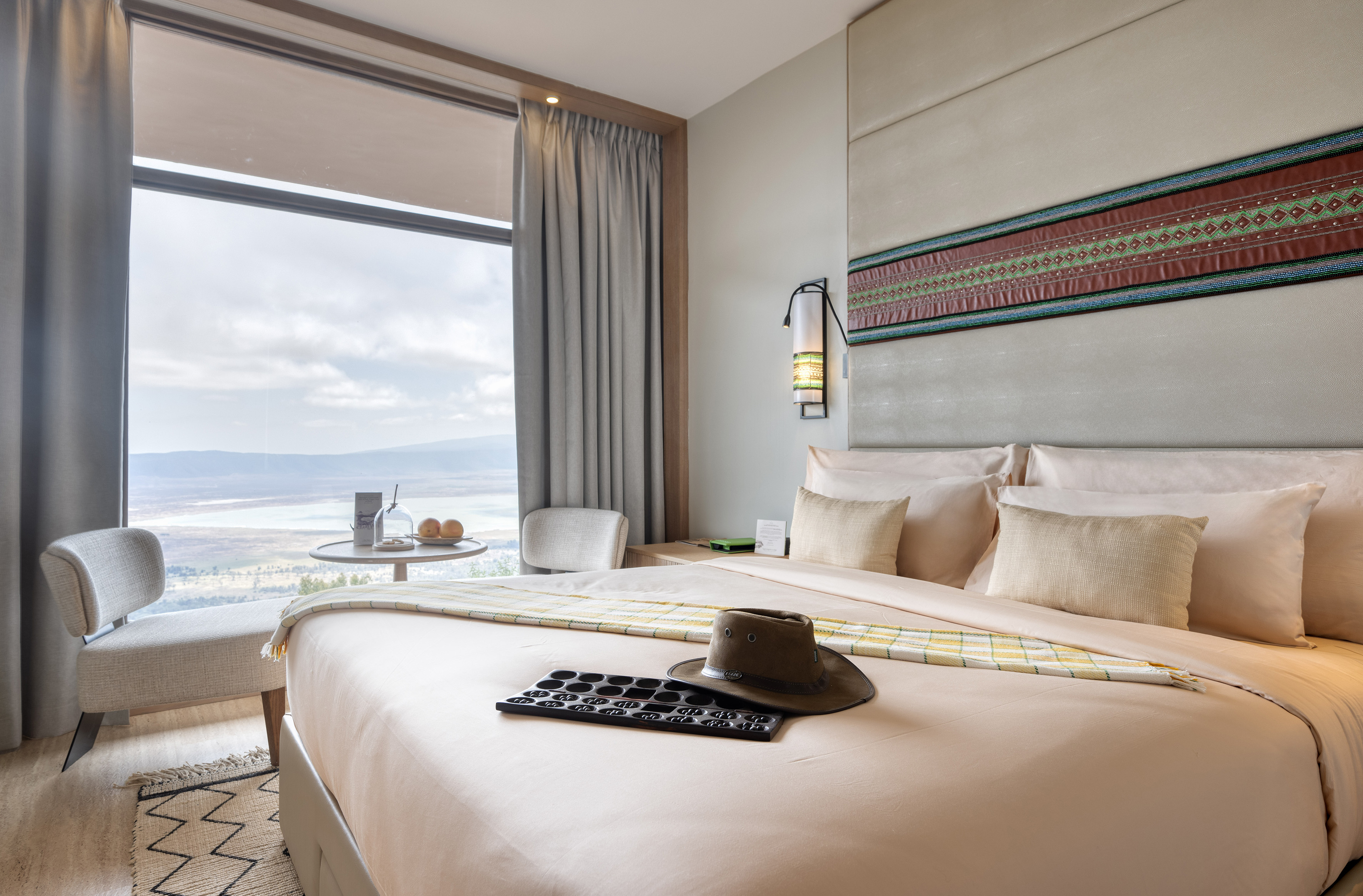 Luxury hotel bedroom with scenic lake view, safari hat, and Mancala game.