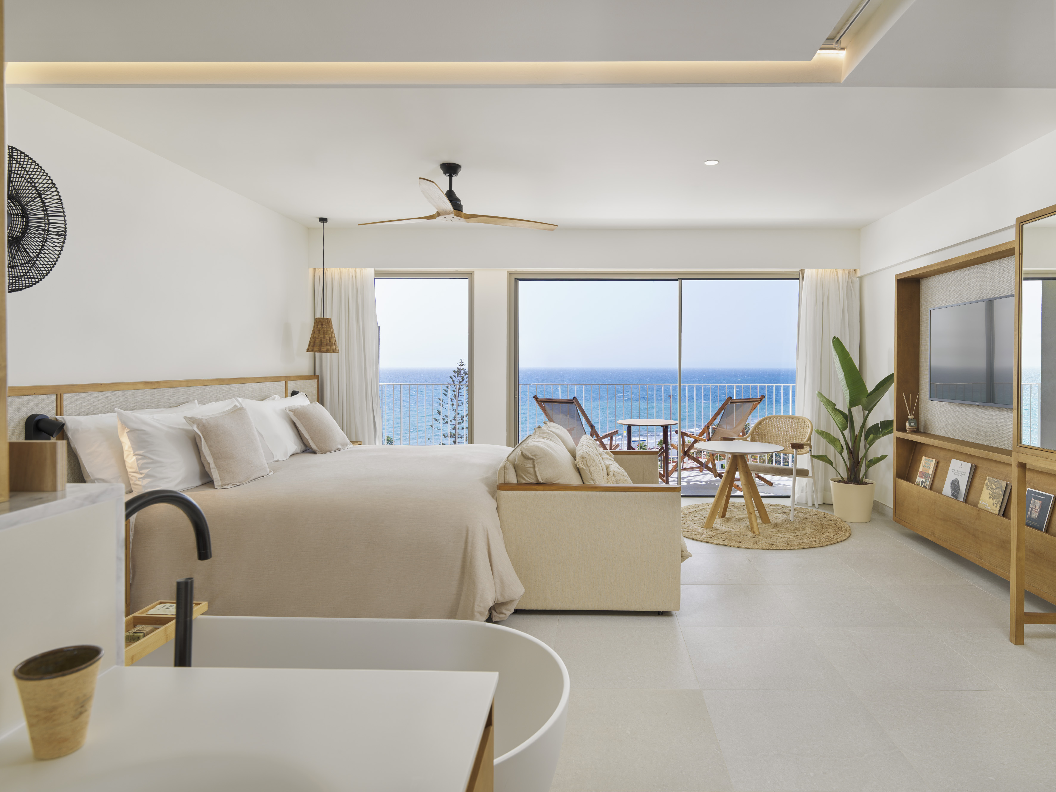 Modern oceanfront hotel bedroom with private balcony and integrated bathtub.