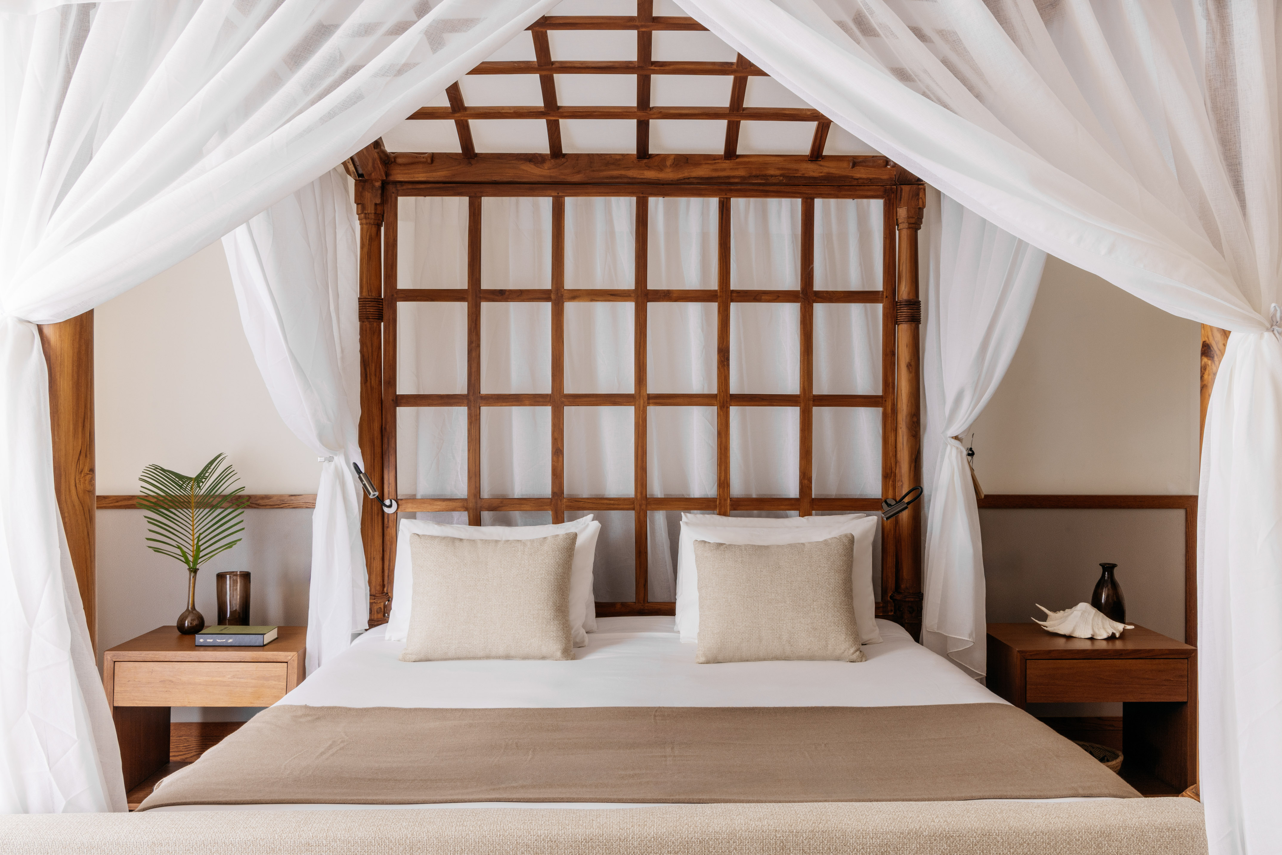 Tropical wooden canopy bed with white drapes, grid headboard, and bedside tables.