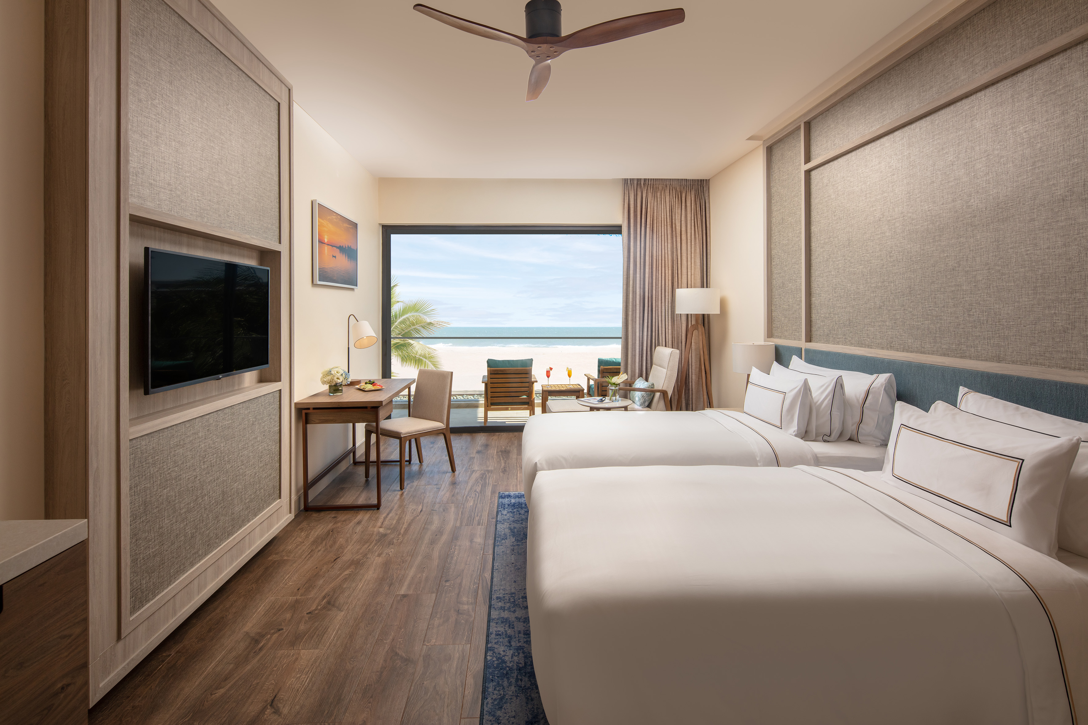 Modern hotel room with two beds, work desk, and stunning ocean view balcony.