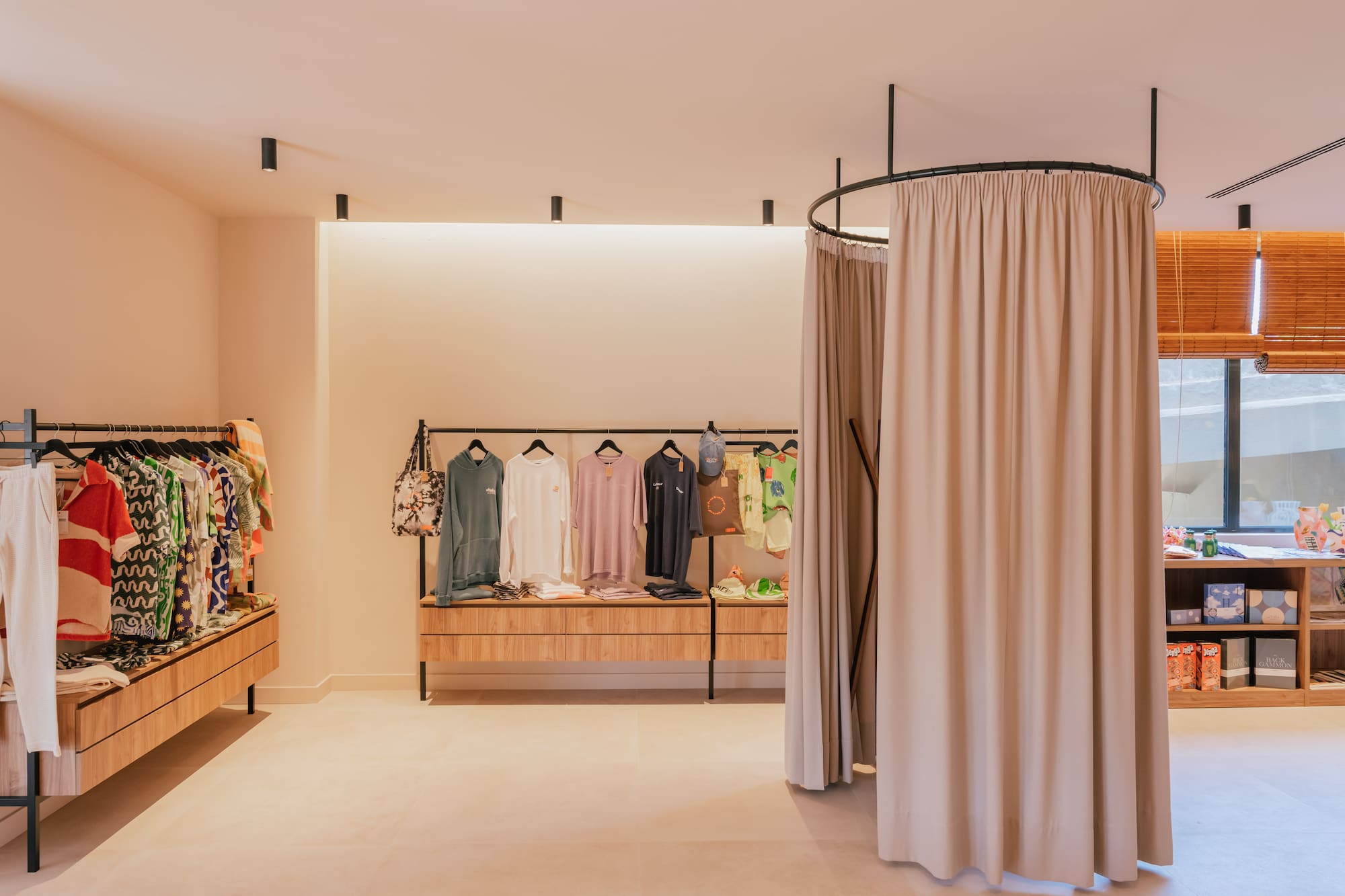 Modern clothing boutique with apparel on display racks and a fitting room.