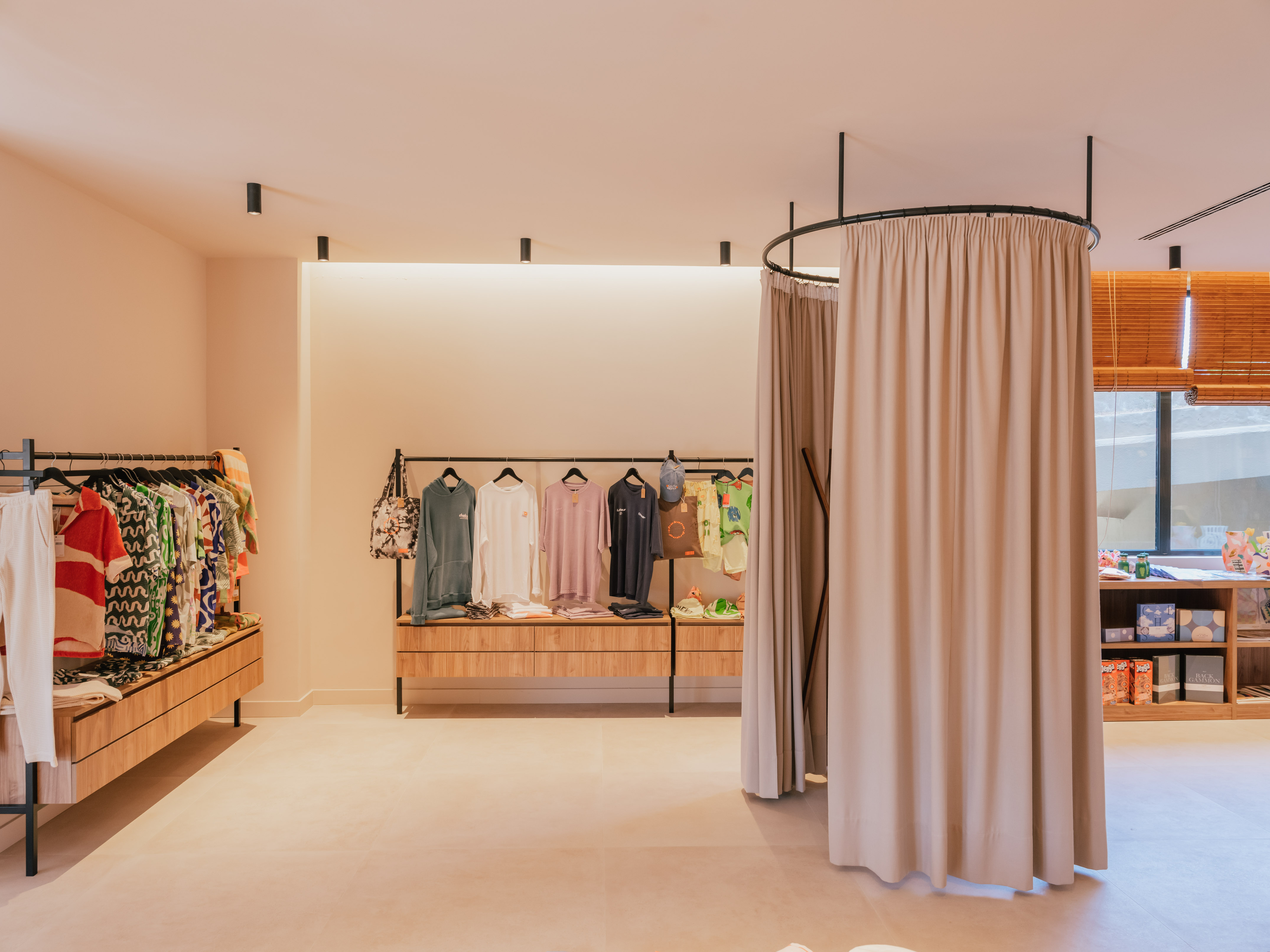 Modern clothing boutique with apparel on display racks and a fitting room.