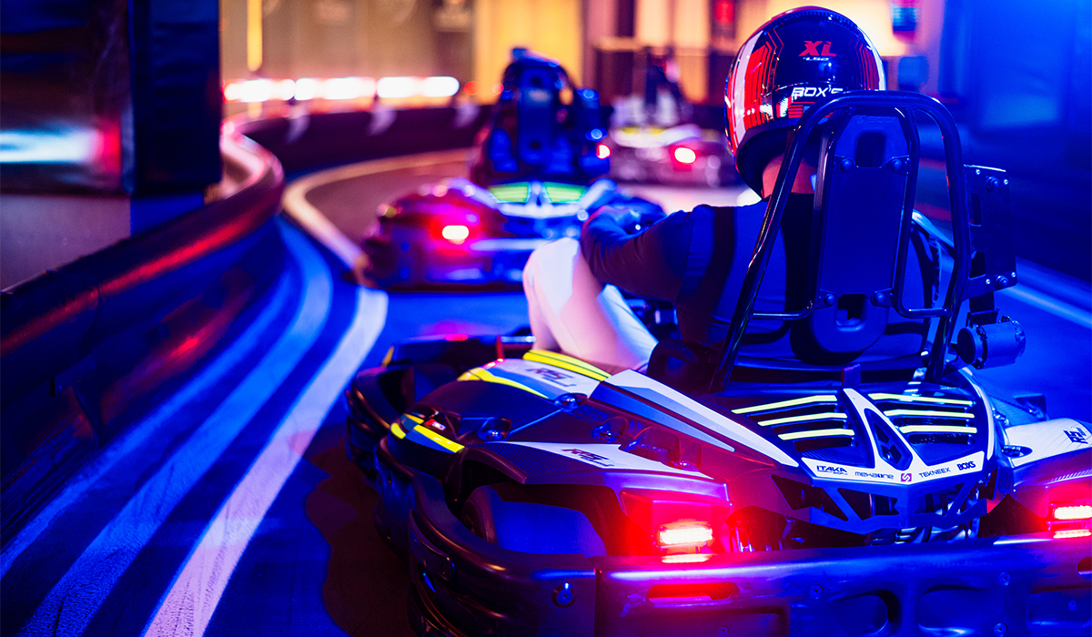 Driver in a helmet on a go-kart, racing on a neon-lit indoor track.