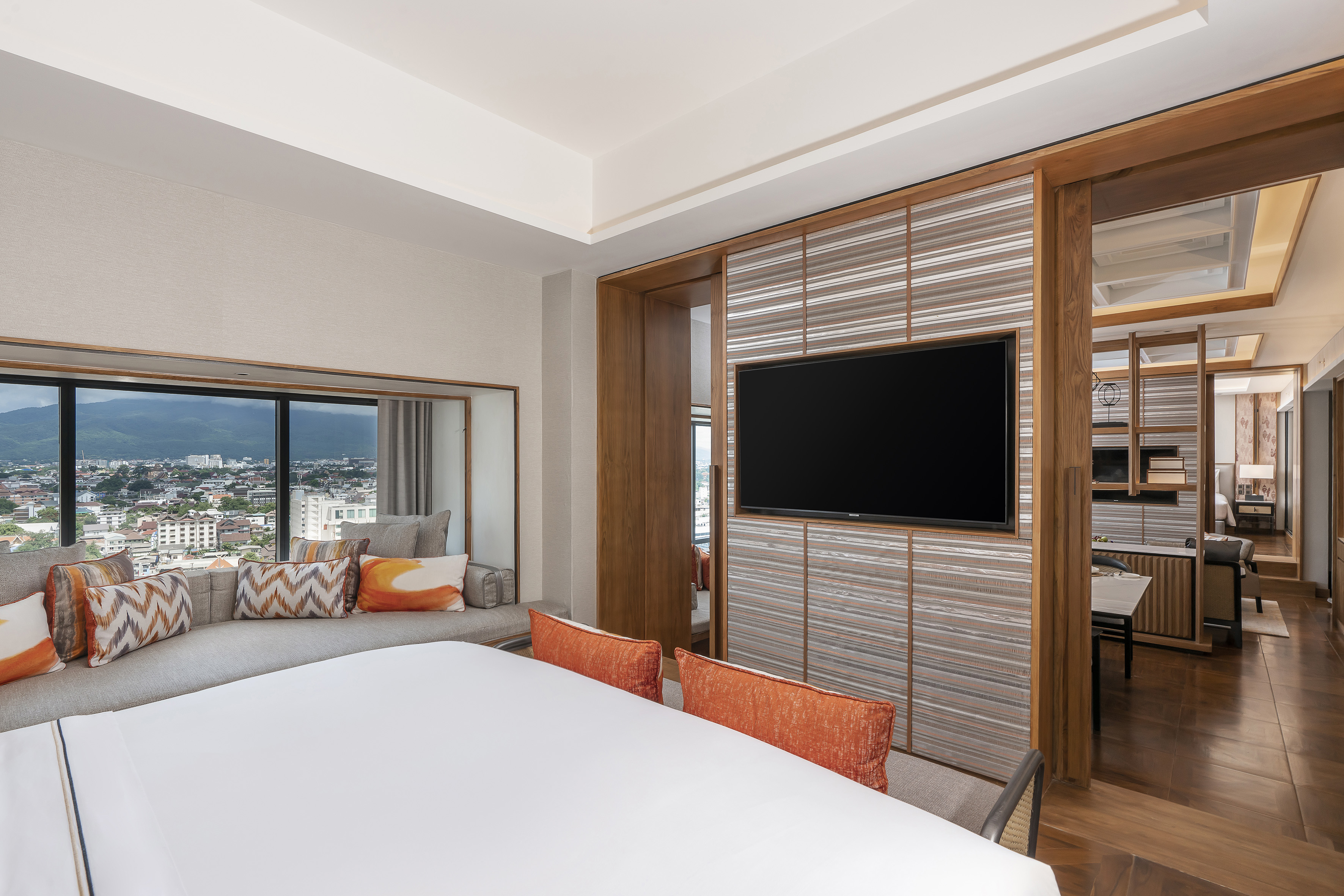 Luxury hotel room with panoramic city and mountain views, bed, window lounge, and TV.