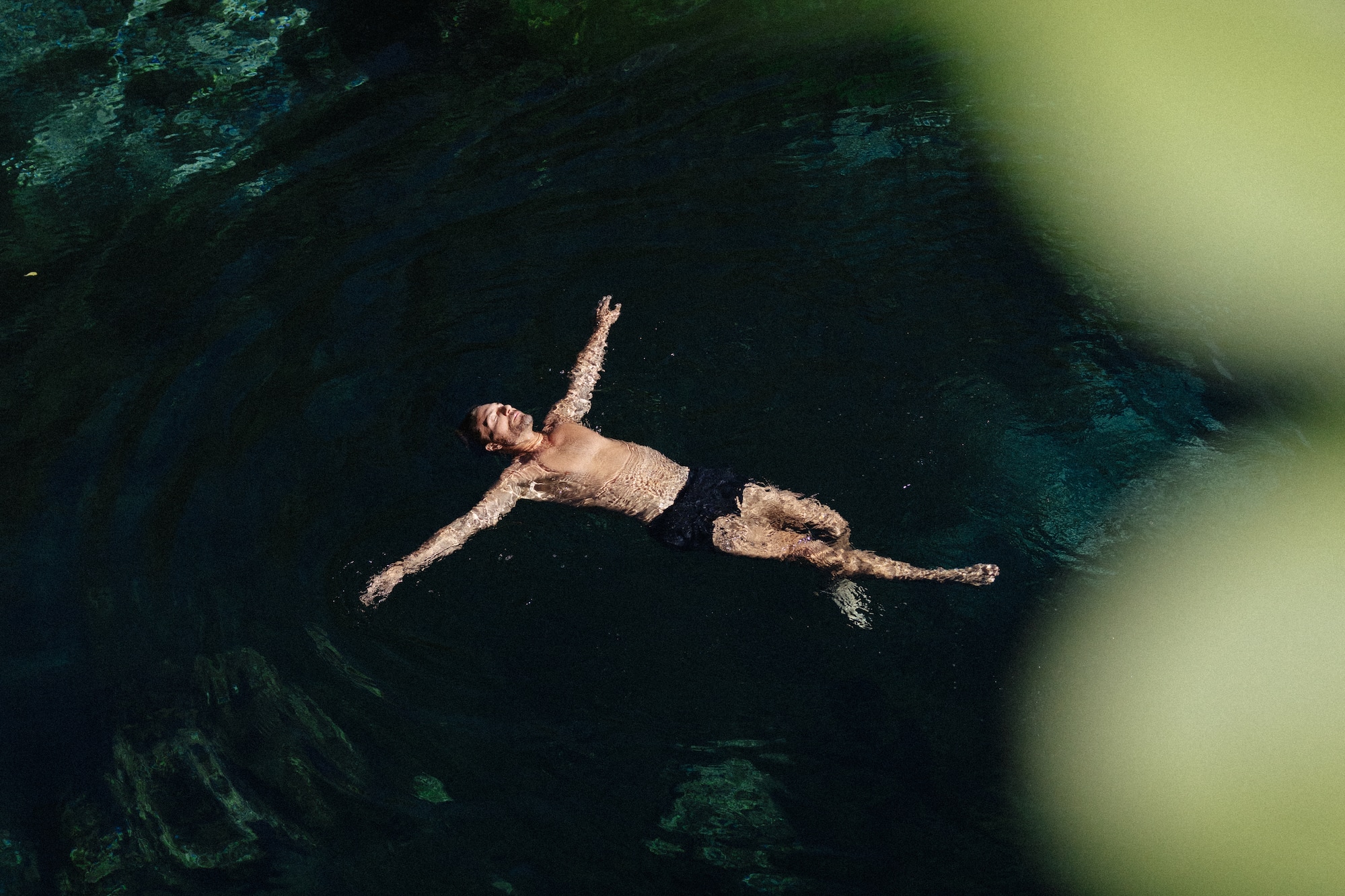 Aerial view of man floating peacefully in dark, clear natural water.