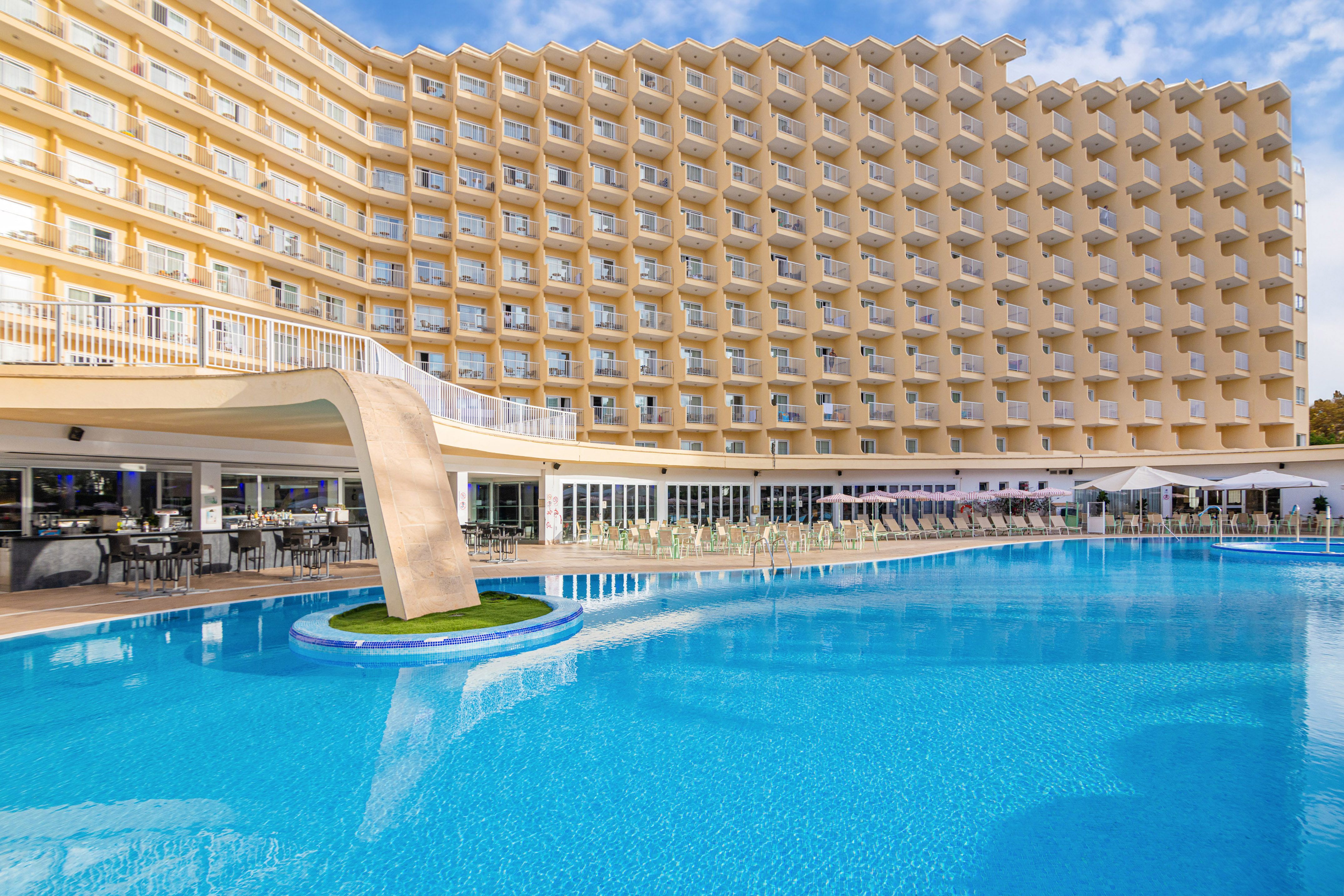 Modern yellow hotel facade with white balconies, blue sky.