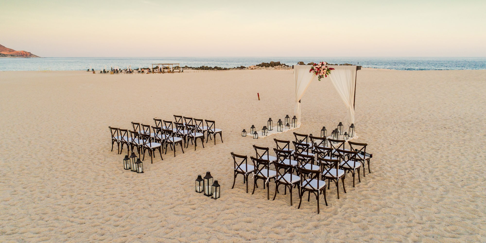 Destination beach wedding setup with floral arch, chairs, and lanterns. - Romance by Paradisus - Paradisus Los Cabos - Adults Only, Los Cabos