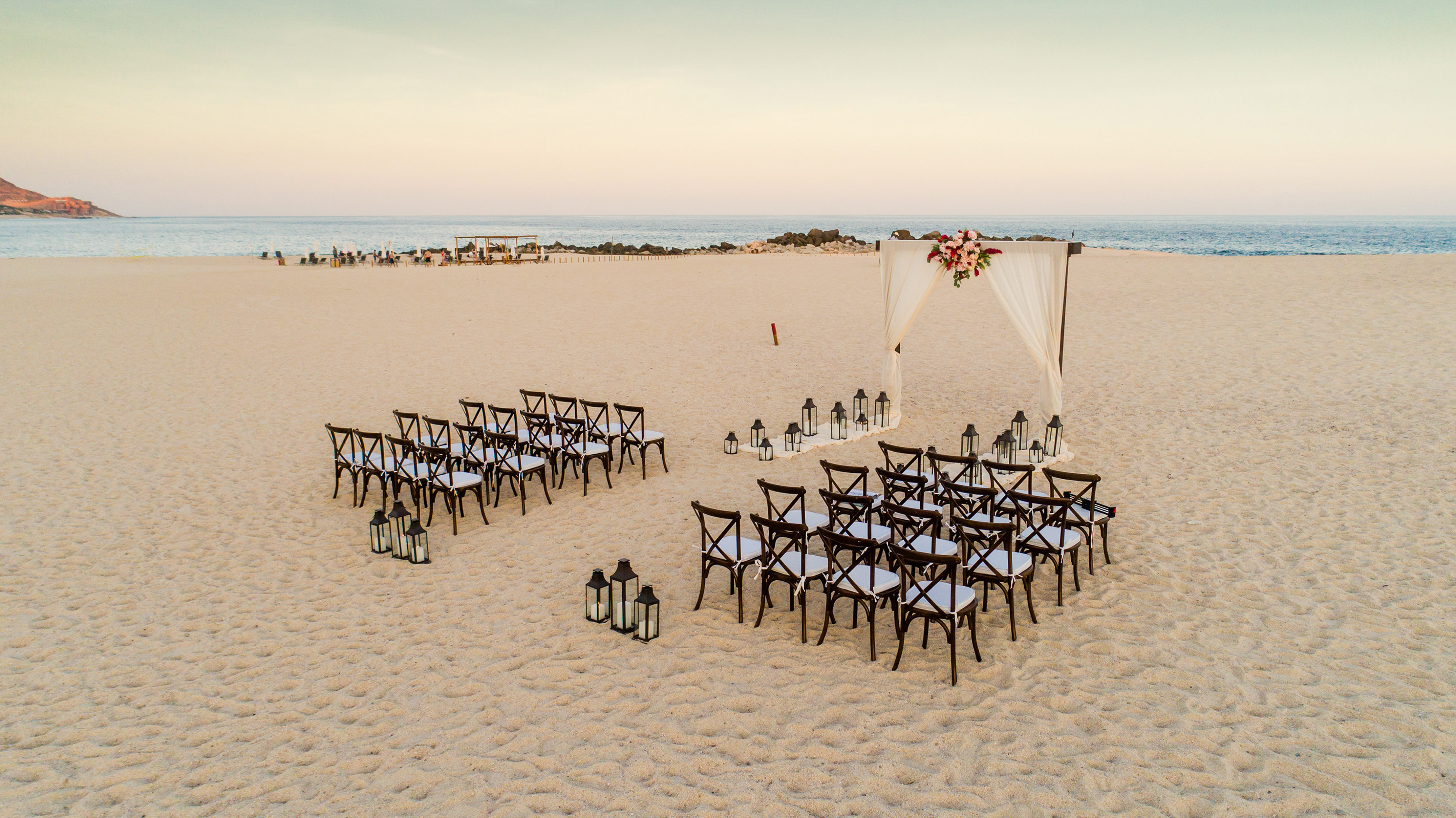 Destination beach wedding setup with floral arch, chairs, and lanterns. - Romance by Paradisus - Paradisus Los Cabos - Adults Only, Los Cabos