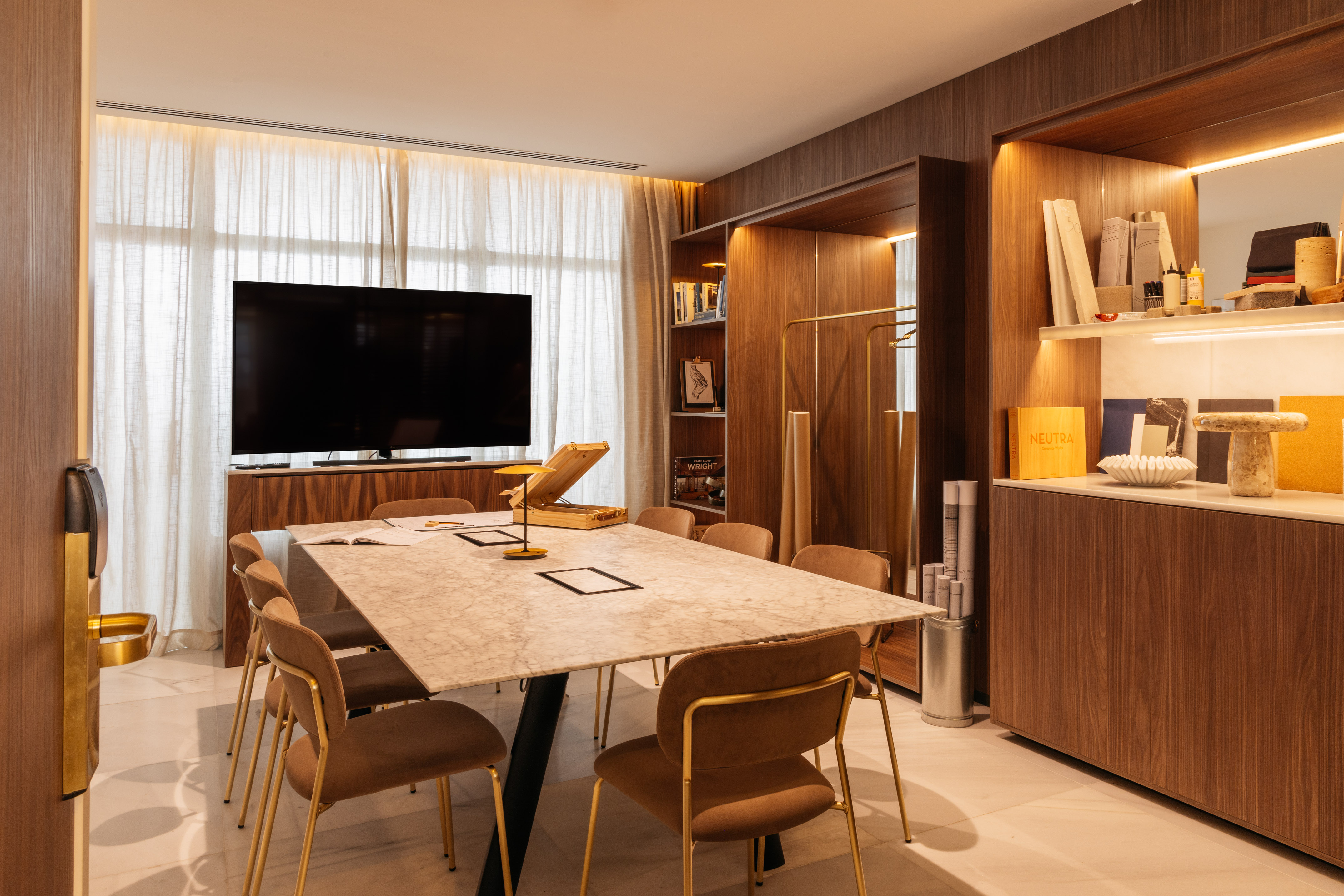 Contemporary meeting room with marble table, brown chairs, TV, and wooden cabinetry.