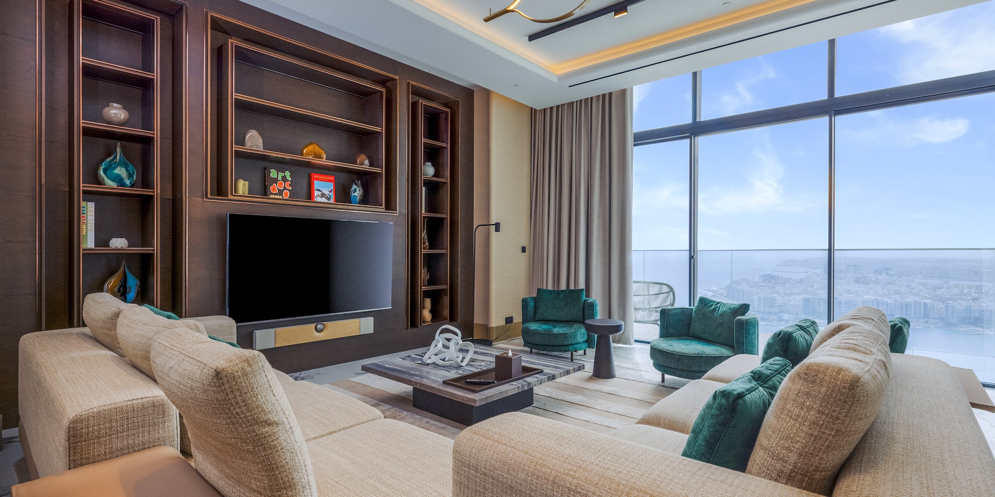 Contemporary living room with beige sofa, green armchairs, media wall, and city view.
