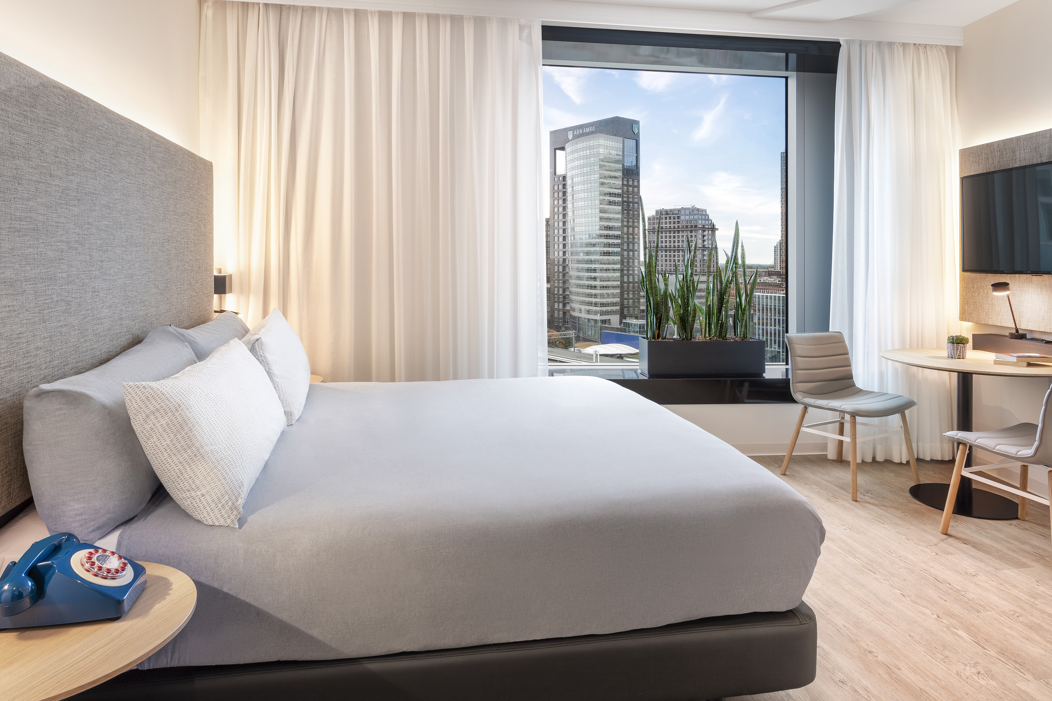 Hotel room with city skyline view, comfortable bed, and a functional workspace.