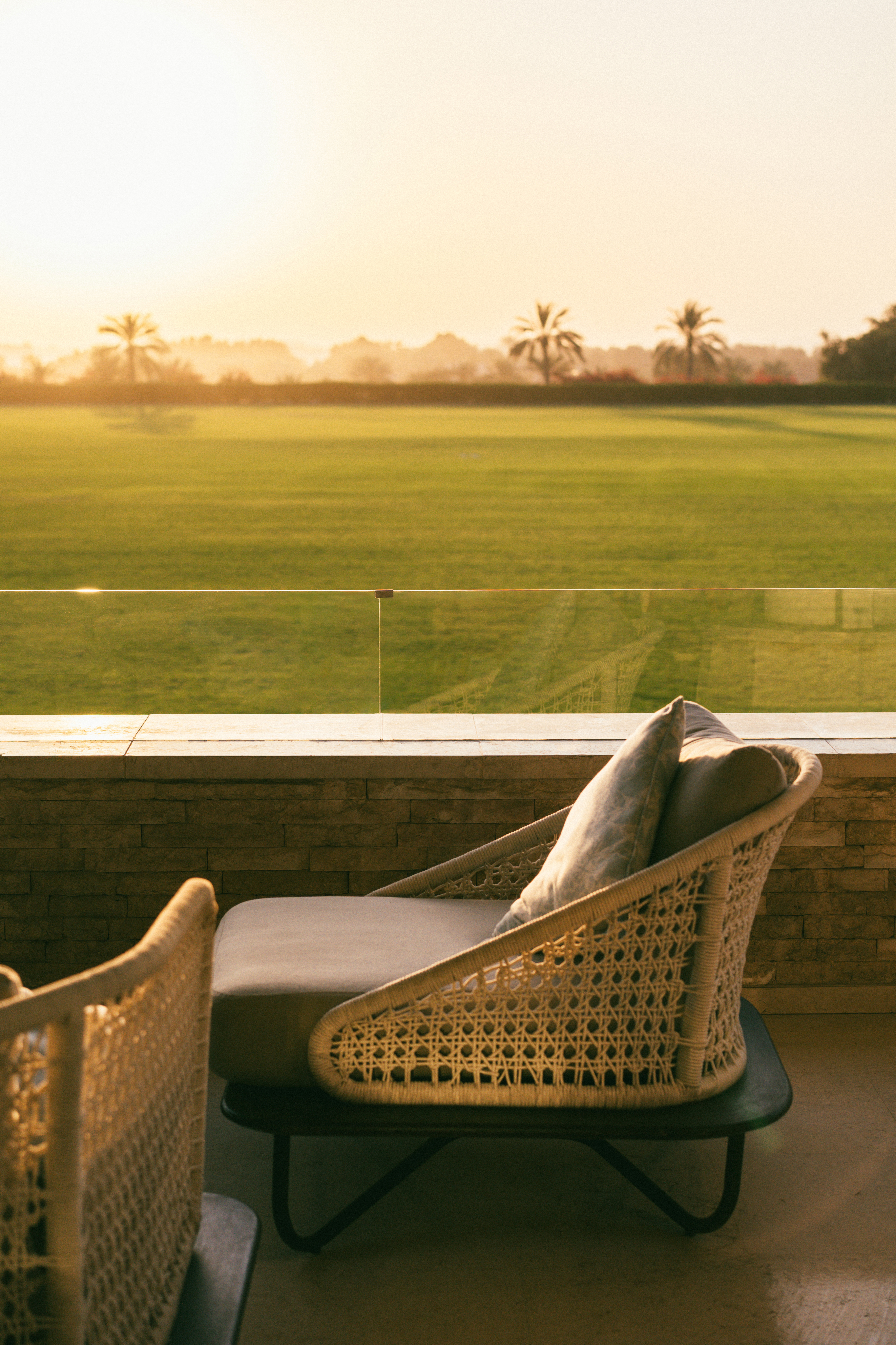 Resort balcony with wicker lounge chair overlooking a golf course at sunrise.